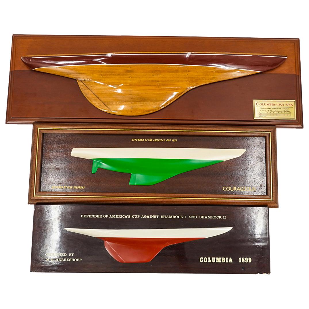 (3 Pc) Mounted Half Hull Nautical Ship Models: DESCRIPTION: Three painted half hull ship models: one of the Courageous, designed by Olin Stephens and defender of the America's Cup in 1974; one of the America; one of the 1899 Columbia designed by N