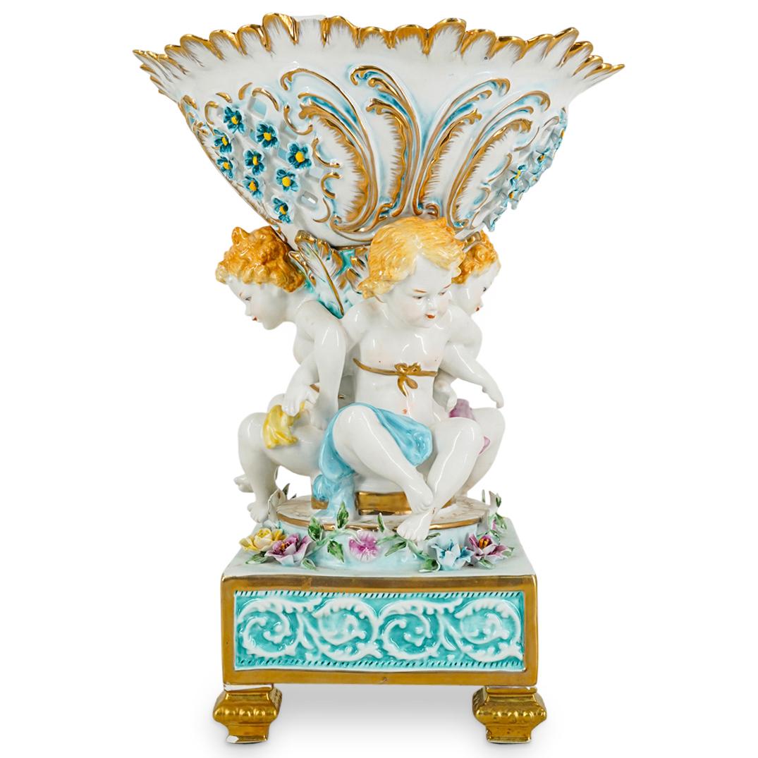 Limoges Porcelain Reticulated Putto And Floral Centerpiece: DESCRIPTION: Limoges porcelain centerpiece featuring a reticulated bowl decorated with delicate flower designs and motifs and supported by a stem composed of three puttos linking arms while seated amo