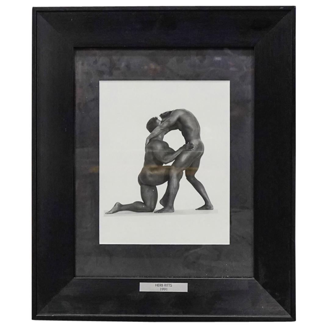 After Herb Ritts (1952-2002) Print From Duo Series: DESCRIPTION: After Herb Ritts erotic print from the Duo series depicting two men kissing in bending and kneeling positions. Framed in a black frame adorned with a silver plaque emblazoned "HERB RITTS 