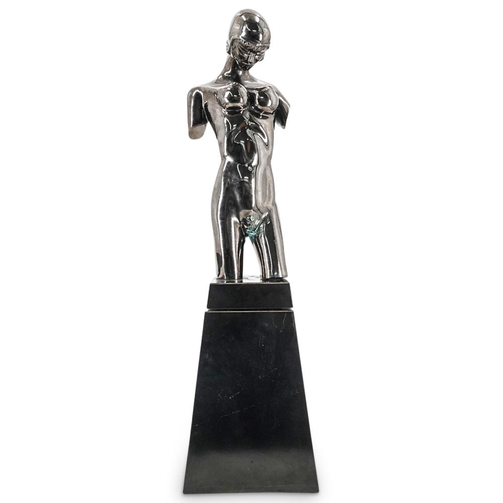 Ronald Goodman (American) Stainless Nude Bronze: DESCRIPTION: Silver stainless sculpture depicting a stylized, armless, nude woman wearing a helmet and gazing downwards. Piece is mounted on an obelisk base. CIRCA: 20th Century ORIGIN: Continental DI