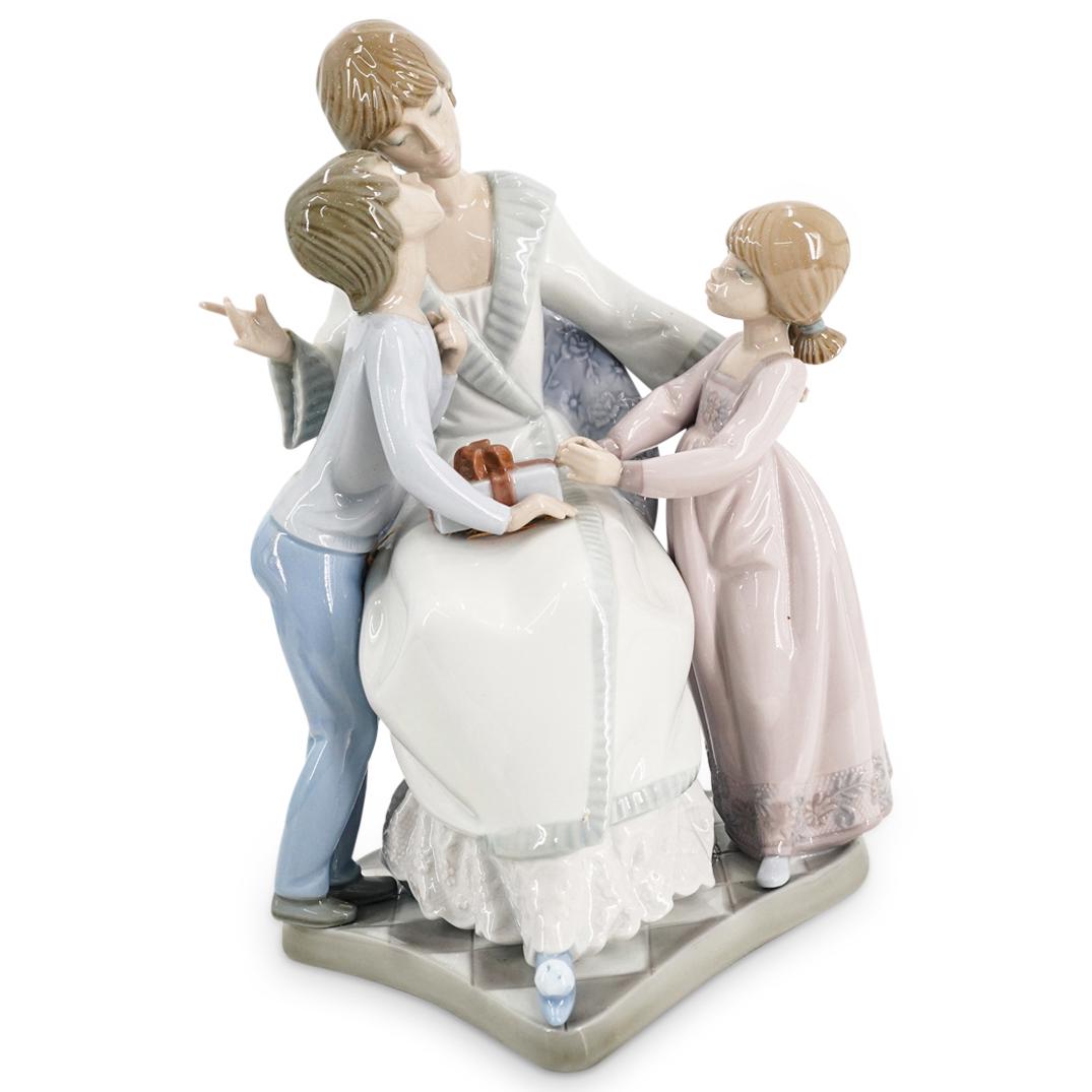 Lladro "A Gift Of Love" Porcelain Grouping: DESCRIPTION: Lladro porcelain figure entitled "A Gift of Love" ("Dear Mama"/ "Querida Mama") designed by Francisco Catala depicting a son and daughter giving a wrapped gift to their seated mother. Pie