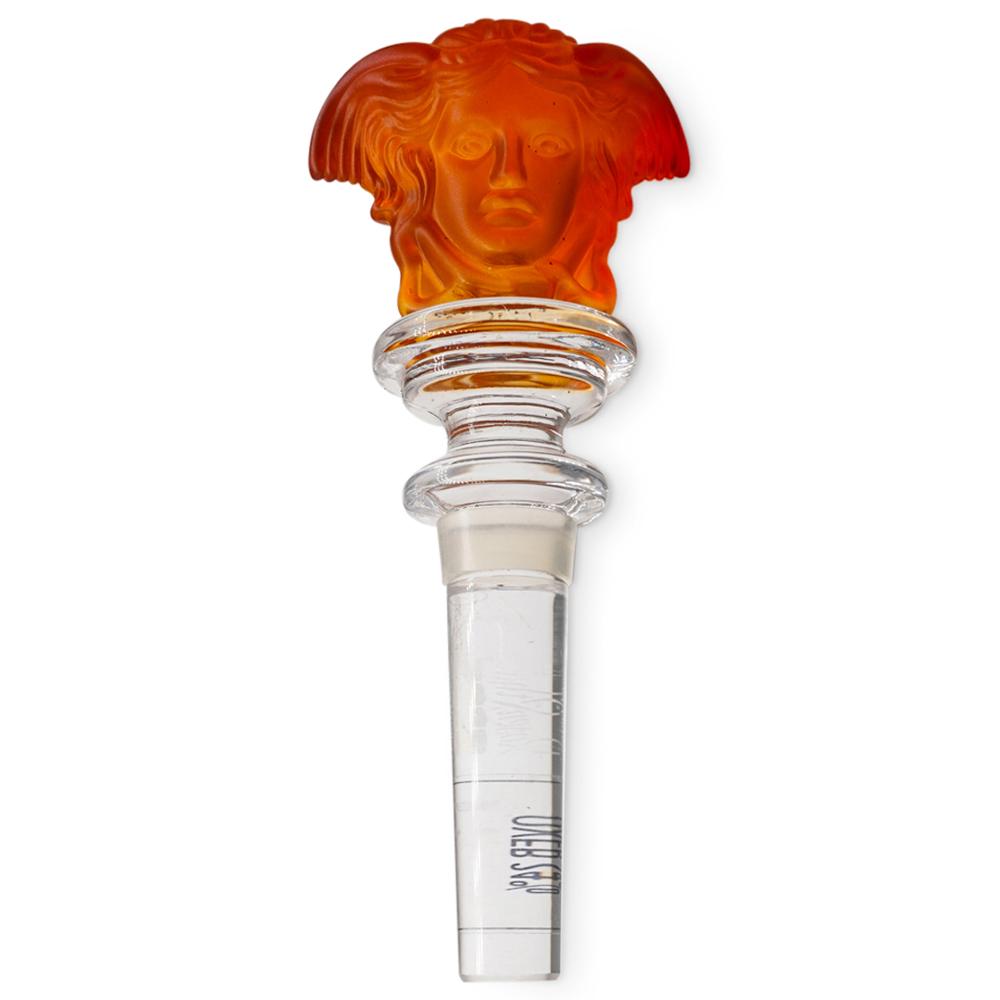 Rosenthal Versace Medusa Head Stopper: DESCRIPTION: A Rosenthal Versace stopper featuring an amber colored head of Medusa along the top and clear crystal along the stem. Marked: "Rosenthal Versace". With original box. CIRCA: 20th Century.