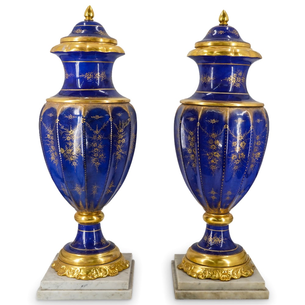 Pair French Porcelain Blue Glazed And Gilt Accented Urns: DESCRIPTION: Two matching porcelain urns, each composed of five segments held together and mounted on an alabaster base by a long bolt. Each piece is coated in a blue glaze accented with gilt flowers