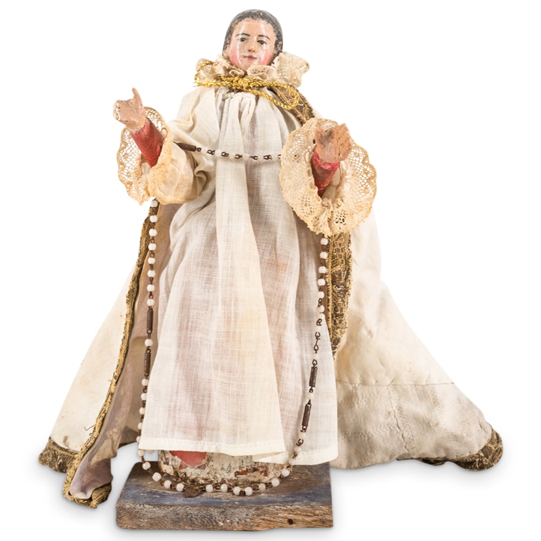 Antique South American Robed Wooden Saint: DESCRIPTION: Antique carved wooden saint dressed in a white robe with lace hems at the sleeves and covered with a gilt hemmed mantle tied with a gilt stringed bow. Finished with a rosary draped over a