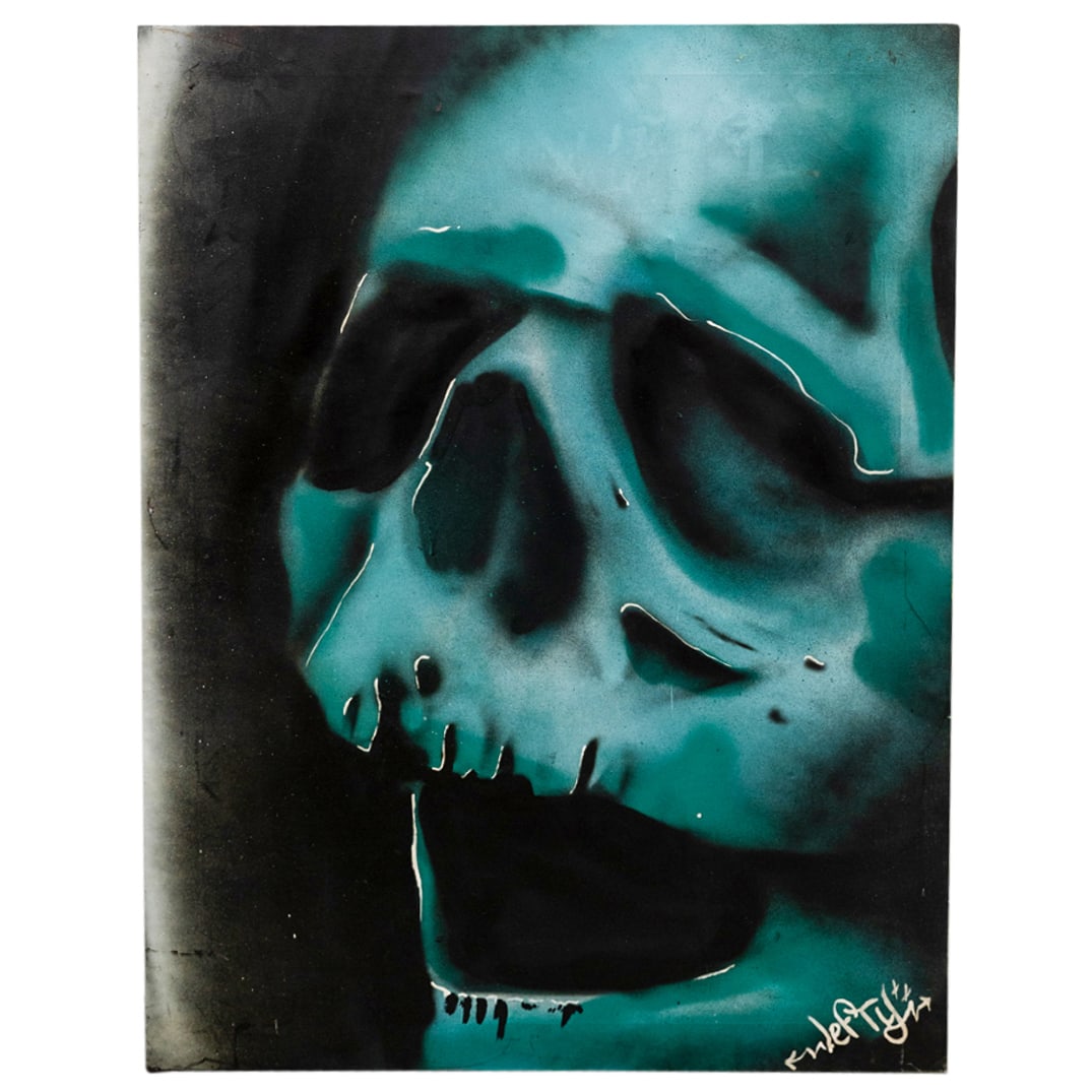 Signed Lefty Blue Green Skull Spray Paint On Canvas: DESCRIPTION: Spray paint on canvas painting depicting a blue green skull against a black background. Signed with artist's tag "Lefty" at lower right; additional tag-like marks present on verso. CIRCA: