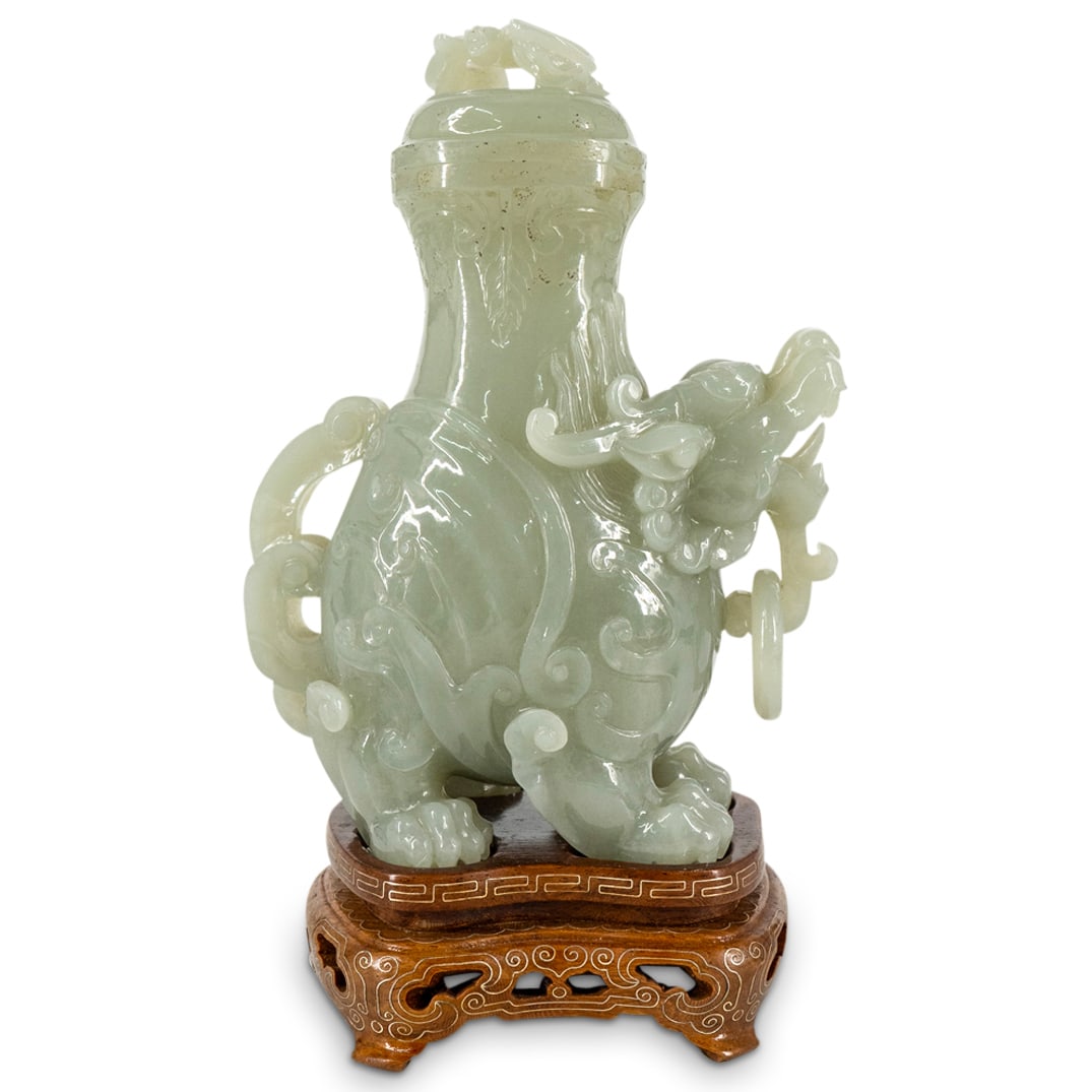Antique Chinese Jade Pixiu Urn On Stand: DESCRIPTION: Antique Feng Shui urn carved from jade and crafted as a double horned pixiu bearing a loose ring on her beard and a bat atop the lid on her back. Includes carved wooden stand inlaid with