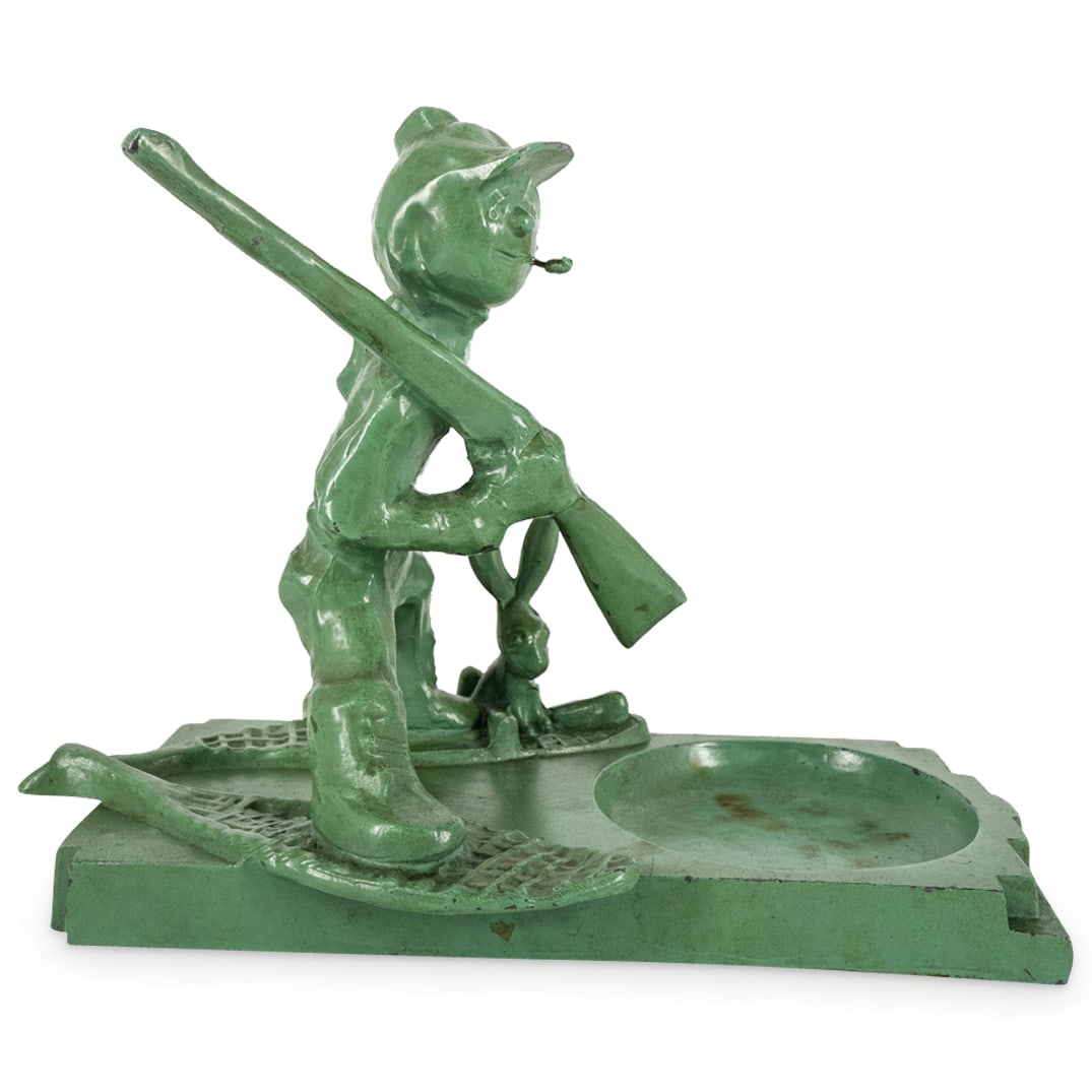 Art Deco Frankart Hunter Ashtray: DESCRIPTION: Art Deoc ashtray by Frankart featuring a sculpture on one side depicting a hunter wearing snowshoes, bearing a rifle, and accompanied by a rabbit. Finished with painted verdigris tone coa