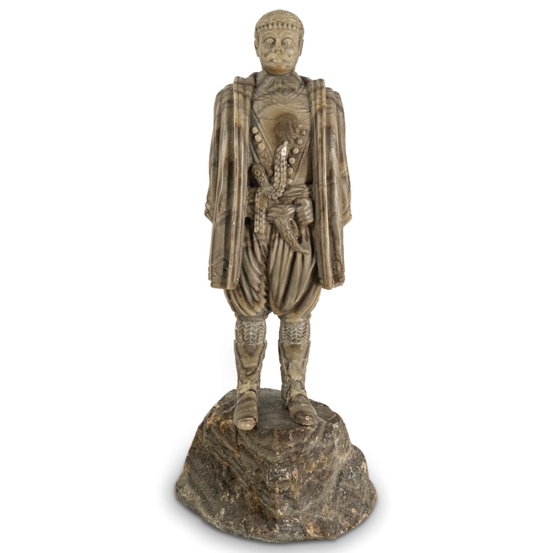 Caucasian Ethnic Military Carved Stone Figural Sculpture: DESCRIPTION: Caucasian Ethnic Military Carved Stone Figural Sculpture. Depicts a standing male figure with a dagger, wearing a knee-length over coat and boots, standing atop a carved stone rock format