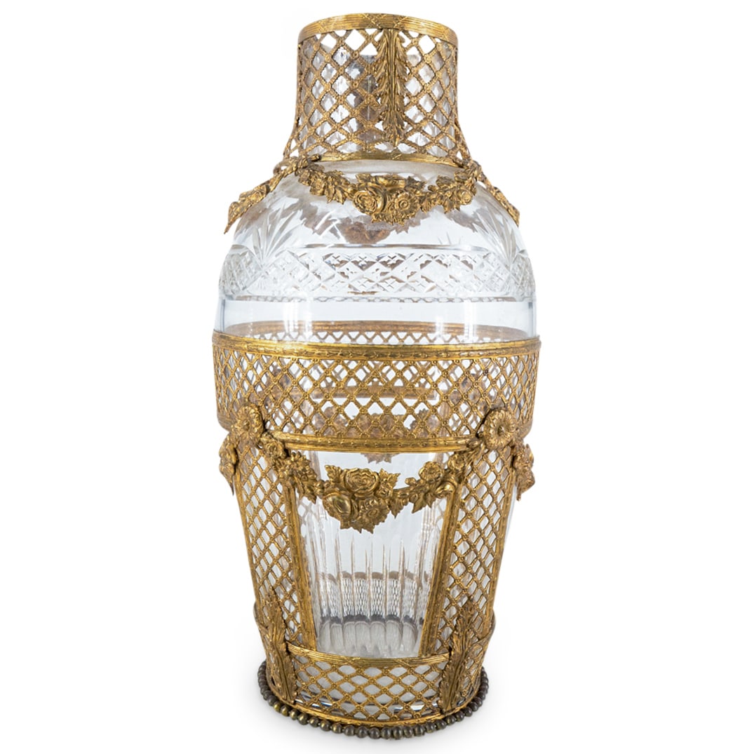 Baccarat Style Brass Mounted Glass Vase: DESCRIPTION: Baccarat style vase featuring a glass body and brass openwork mounts decorated with floral and foliage motifs. CIRCA: Early to mid-20th Century ORIGIN: France DIMENSIONS: H: 13" D: 6.25" 