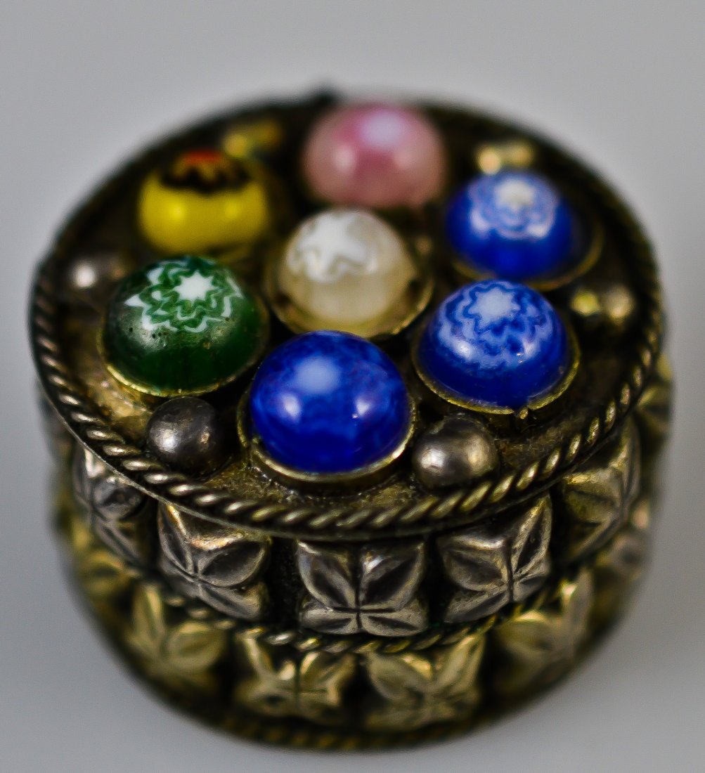 Multi stone and ornate metal pill box: DESCRIPTION: Ornate metal and multi colored stone pill box. Velvet interior lining CIRCA: 1910-1930's MADE IN: China DIMENSIONS: H: 0.75" L: 1.25"