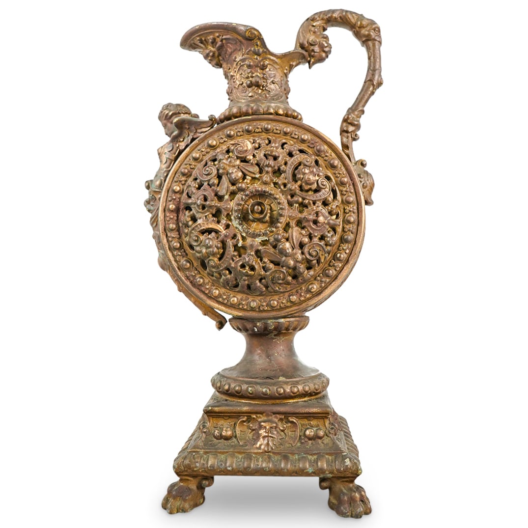 Ornate Cast Metal Repousse Ewer: DESCRIPTION: Ornate cast metal urn ewer with bronze patina finish depicting repousse reticulated motifs in semi relief, a figurative handle, decorated spout and figurative female torso with wings. CIR