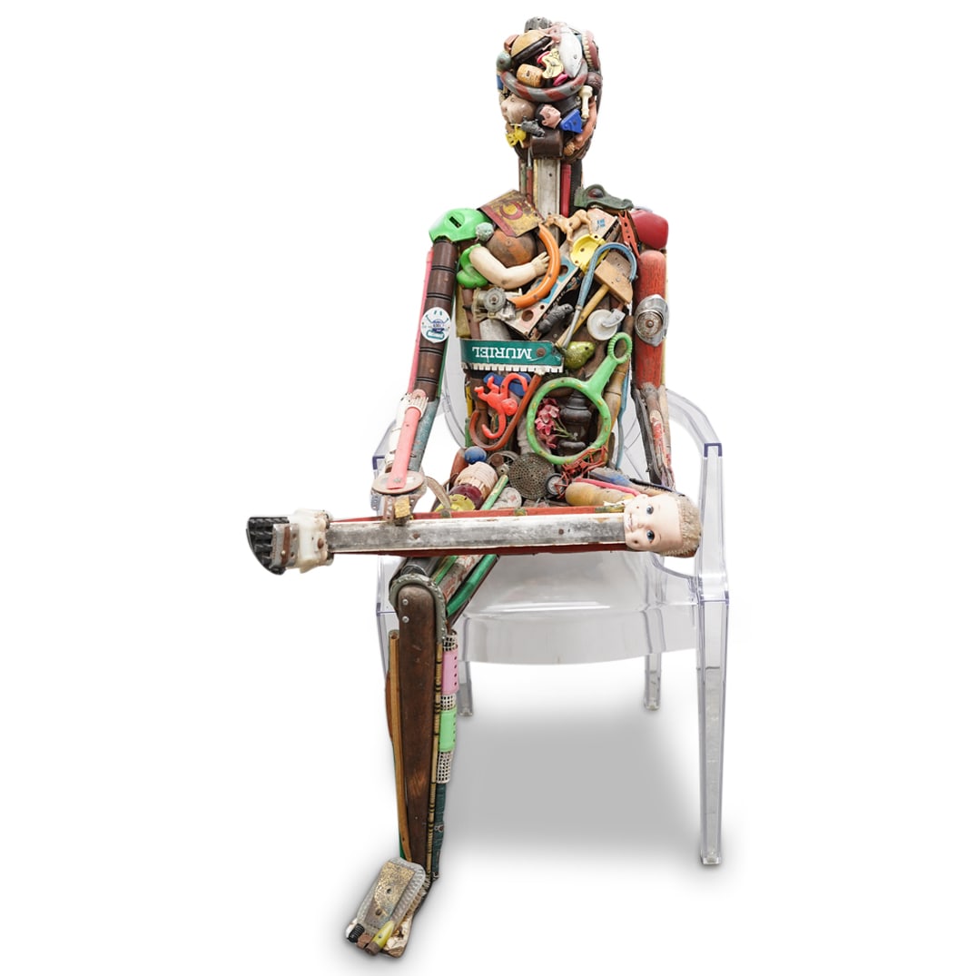 Leo Sewell (B. 1945) Seated Figure: DESCRIPTION: Sculpture by Leo Sewell crafted from various scraps of dolls, toys, signposts, furniture parts, and a plethora of other paraphernalia depicting a nude man seated with his left leg crossed