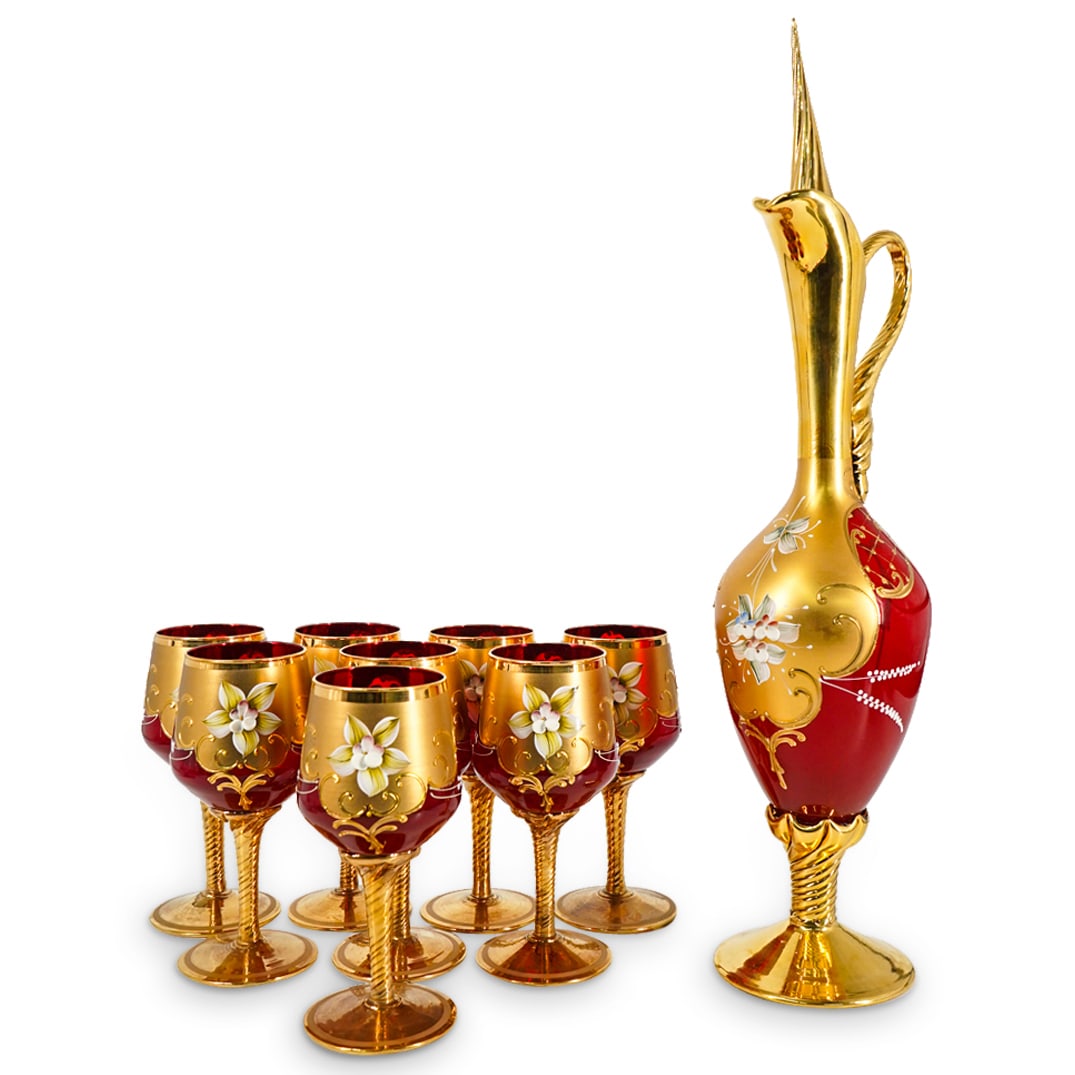 (9 Pc) Vintage Salvadori Murano Ruby Glass and Gilt Wine Set: DESCRIPTION: A set of Murano glass cups features (1) decanter and (8) cups each crafted in a deep ruby red hue and decorated with ornate gilt patterns, further accented with porcelain floral applicati