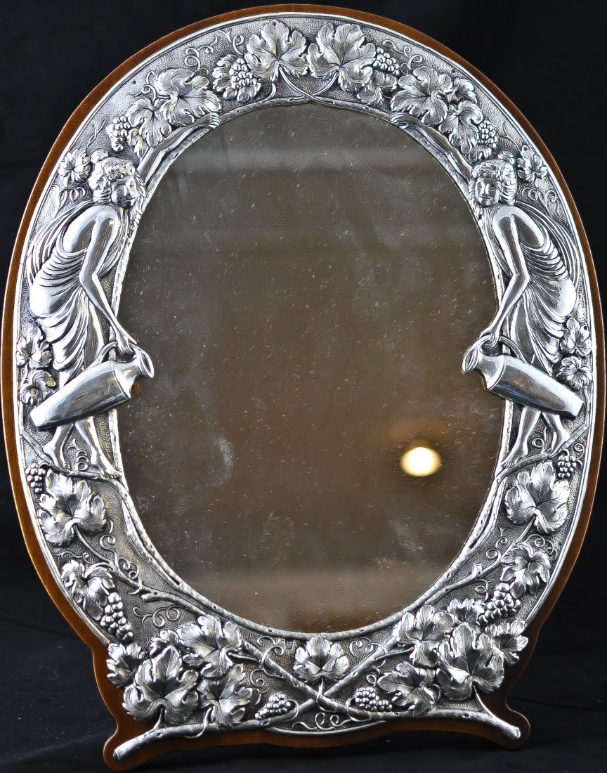 Art Nouveau style Silver mirror. Stamped .950: DESCRIPTION: Art Nouveau style self standing Sterling mirror. Stamped .950. Very ornate raised silver with two women holding water vases adorned by grape plants. Wood backing. Heavy piece. CIRCA: 1960