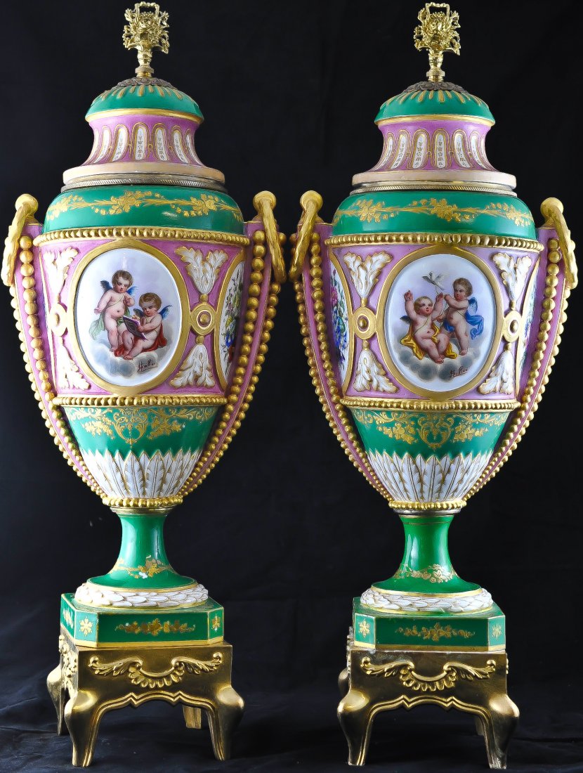 Pair of multi colored porcelain urns by Sevres: DESCRIPTION: Pair of multi colored hand painted porcelain urns by Sevres in a cherub motif, with a gold overlay gilded bronze on the top, as well as the rim of the top. They come on a dore bronze stan