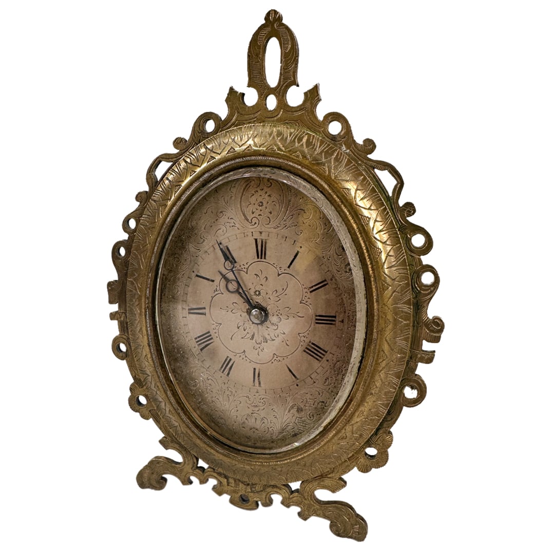 A Strut Clock After Those of Thomas Cole: DESCRIPTION: A strut clock after those of Thomas Cole with a silver face hand dial with painted Roman numerals. The oval case is with a pierced brass. front and an easel back. 4 inches wide x 5 inches