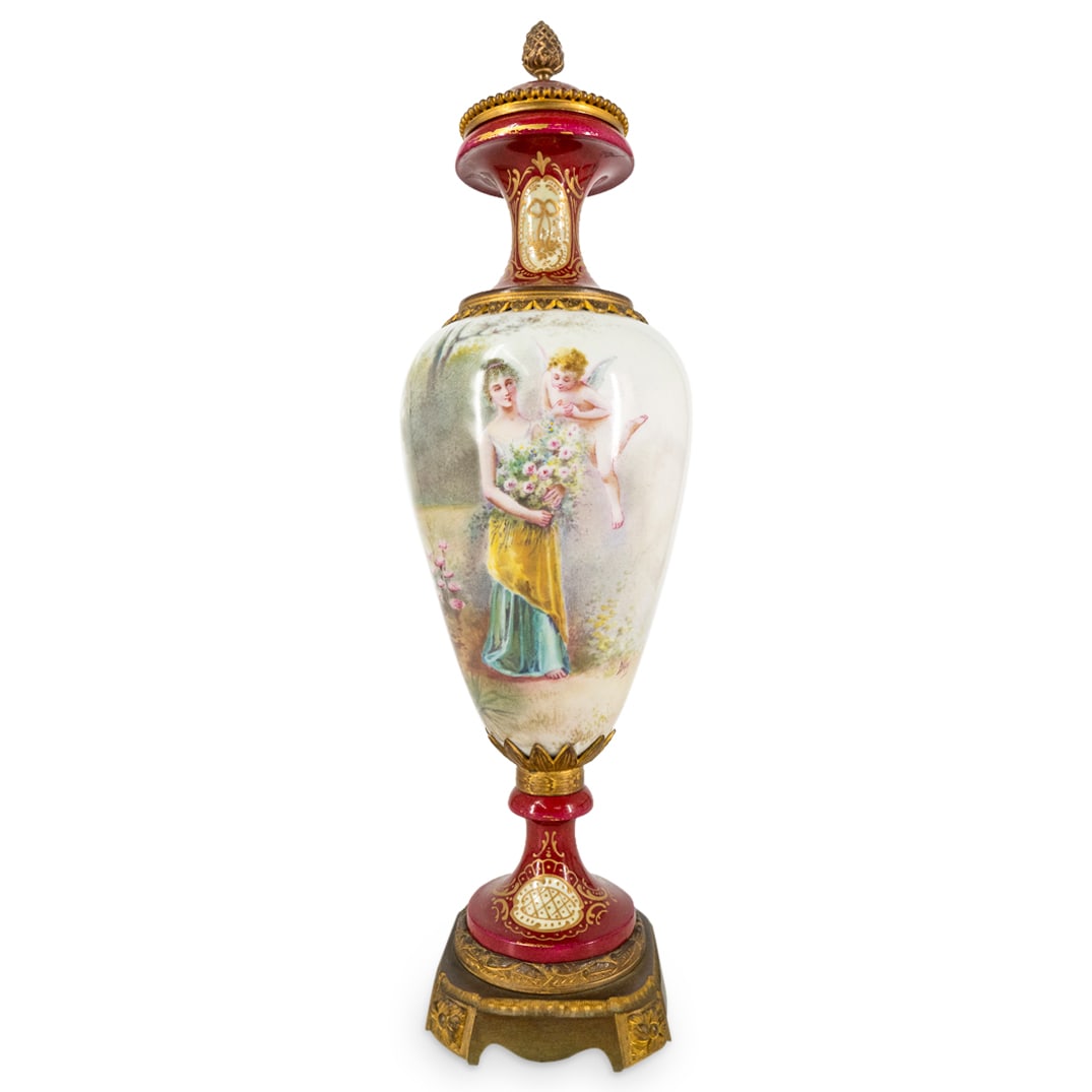 Antique Sevres Style Porcelain Urn: DESCRIPTION: Antiques Sevres style lidded porcelain urn featuring hand painted landscape and scene of woman with Putti. "Daly" at bottom of hand painted scene. Completed with pinecone finial and gilt 