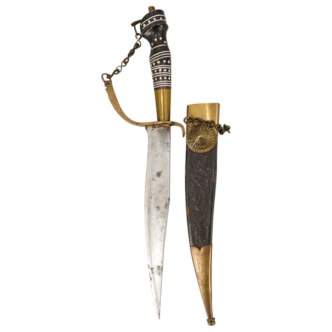 Antique Oriental Brass Mounted Knife In Tooled Leather Sheath: DESCRIPTION: Antique curved steel knife featuring a carved bone handle sporting silver tone accents. Housed in a tooled leather sheath finished with gilt brass trim. CIRCA: Late 19th to early 20th Cen