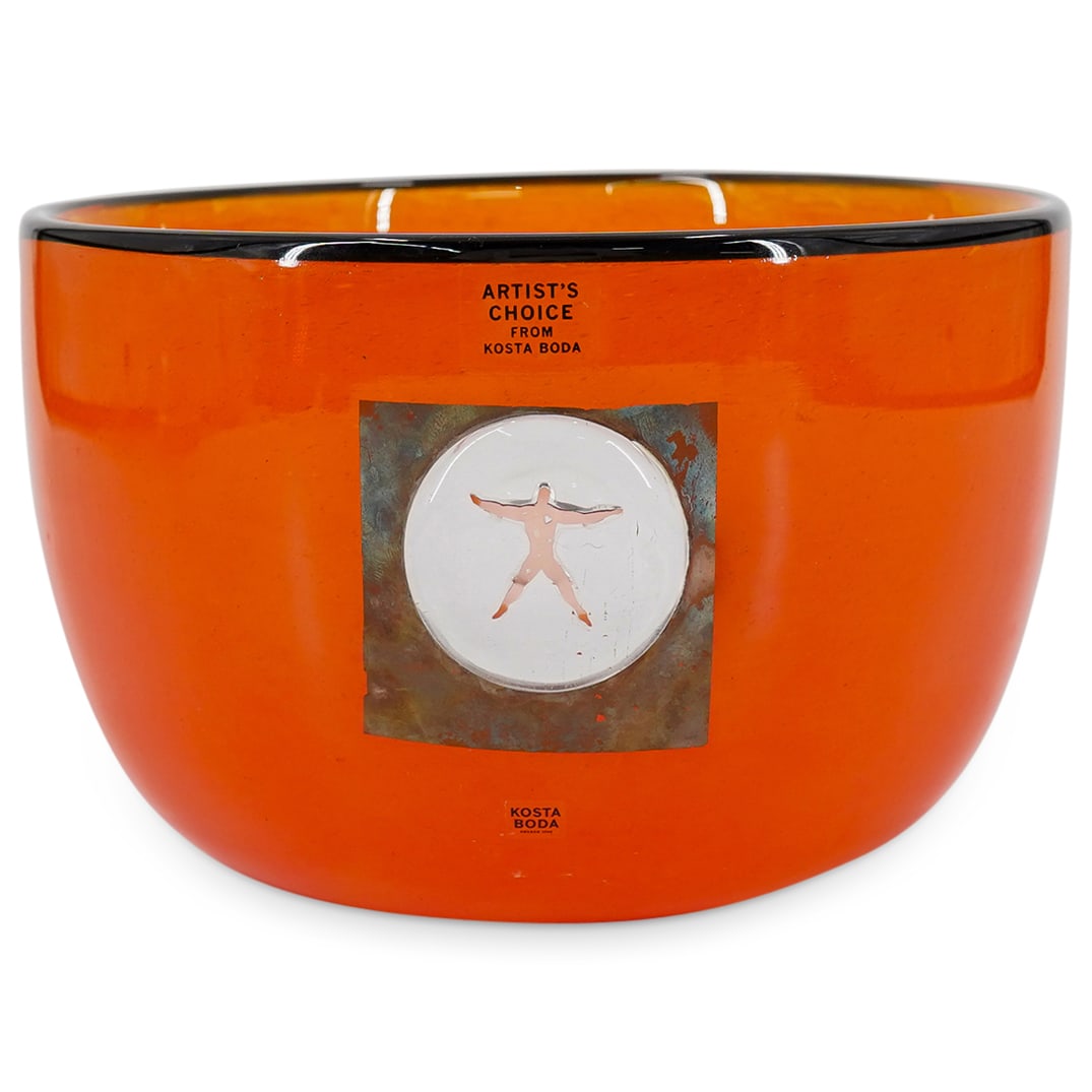 Kosta Boda by Bertil Vallien Art Glass Bowl: DESCRIPTION: Kosta Boda Art Glass bowl with orange color and black rim, designed with applied clear glass over silver figural medallion. Sticker: Artist's Choice From Kosta Boda' Signed: 'Kosta Boda'