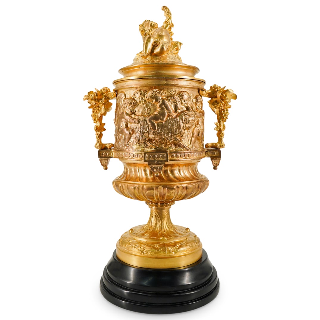 Antique French Dore Bronze Urn: DESCRIPTION: Antique dore bronze urn with cherub finial lid, double grape cluster handles, allegorical reliefs along body, further tapering into an acanthus and laurel leaf decorated foot, and mounted