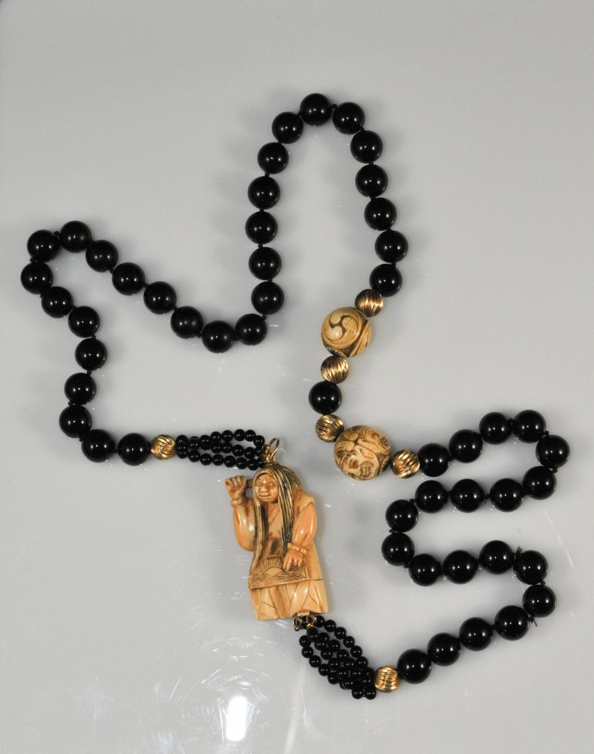 Black onyx beaded necklace with Karakurinetsuke: DESCRIPTION: Large black onyx beaded necklace with Karakurinetsuke. Features a strand of large black onyx beads with a separation of carved ivory balls with faces on it. The other half of the necklace