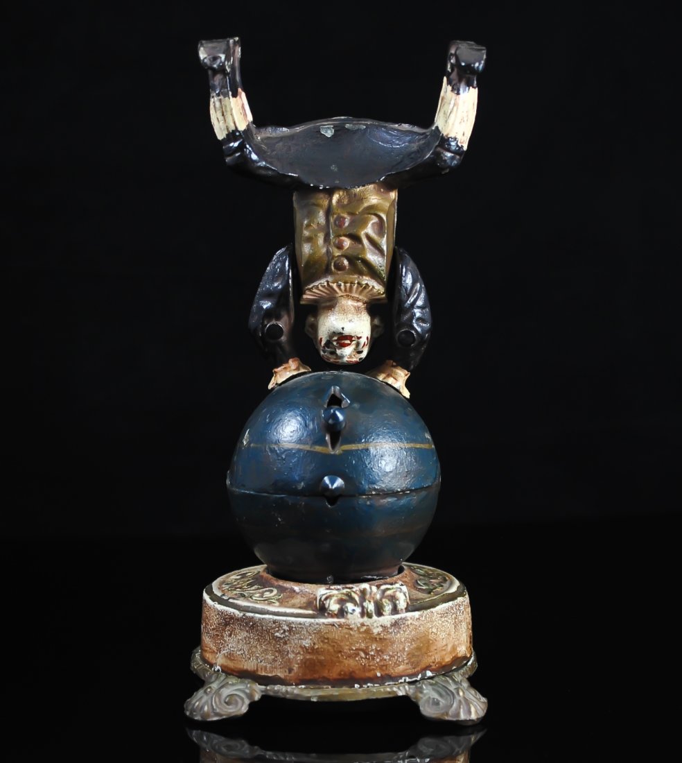 Polychrome pot metal mechanical clown bank: DESCRIPTION: Mechanical pot metal clown coin bank. Features a polychrome panted clown sitting a top a giant ball. There is a lever when released flips the clown upside down into a handstand position. 