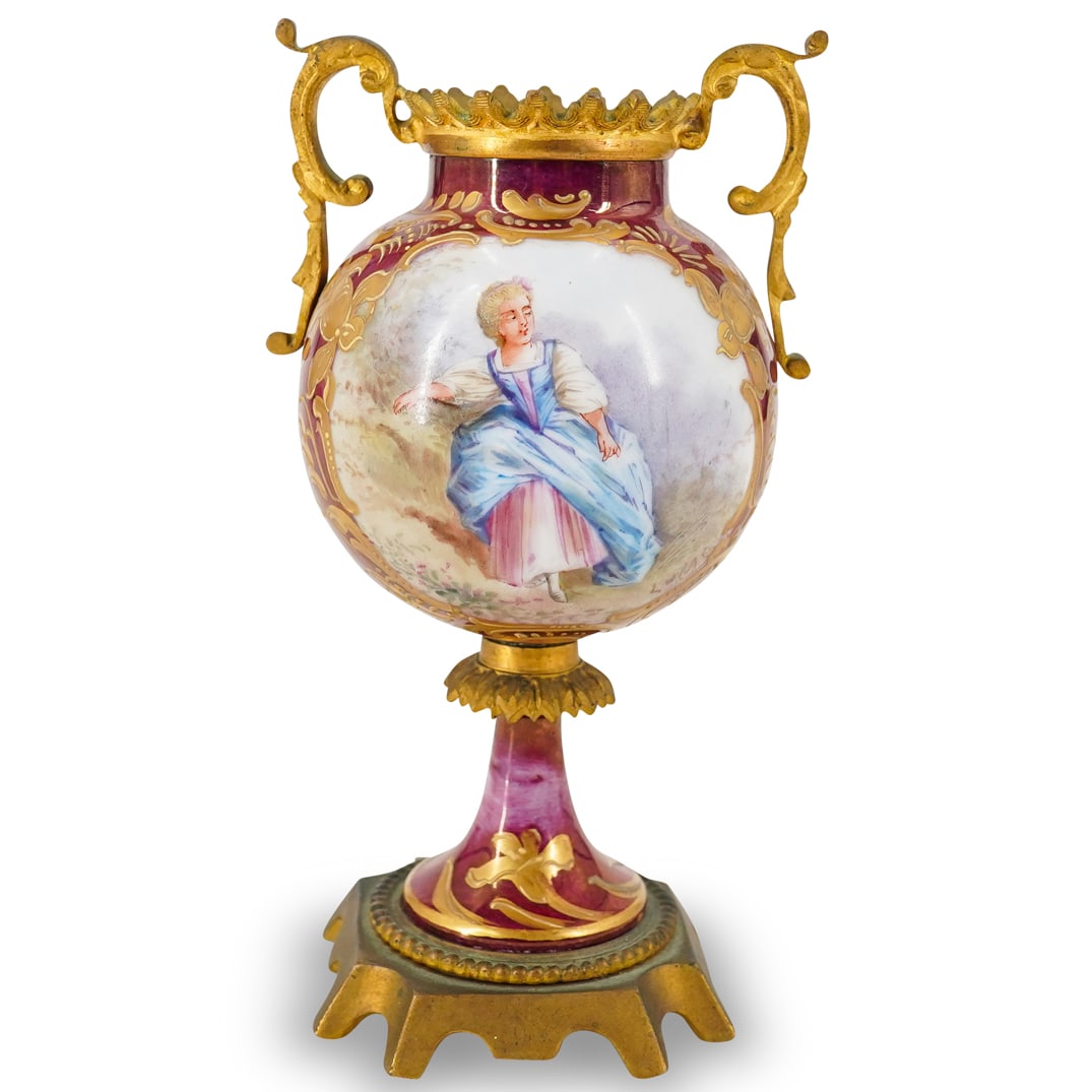Sevres Style Porcelain & Gilt Metal Urn: DESCRIPTION: Small Sevres-style porcelain urn featuring gilt metal fittings, a painted depiction of a woman, and gilt floral and foliage motifs. Signature to lower right of woman. Marked at underside.