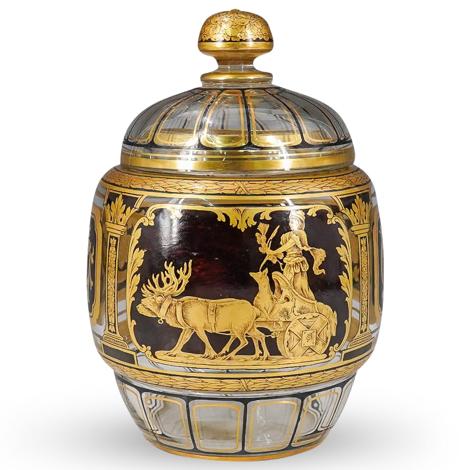 Bohemian Glass Black & Gilt Urn: DESCRIPTION: Bohemian clear glass lidded urn with intricate floral designs on one side, scene with reindeer and wolf pulling robed woman on the other, and gilt accents throughout. Various fruits paint