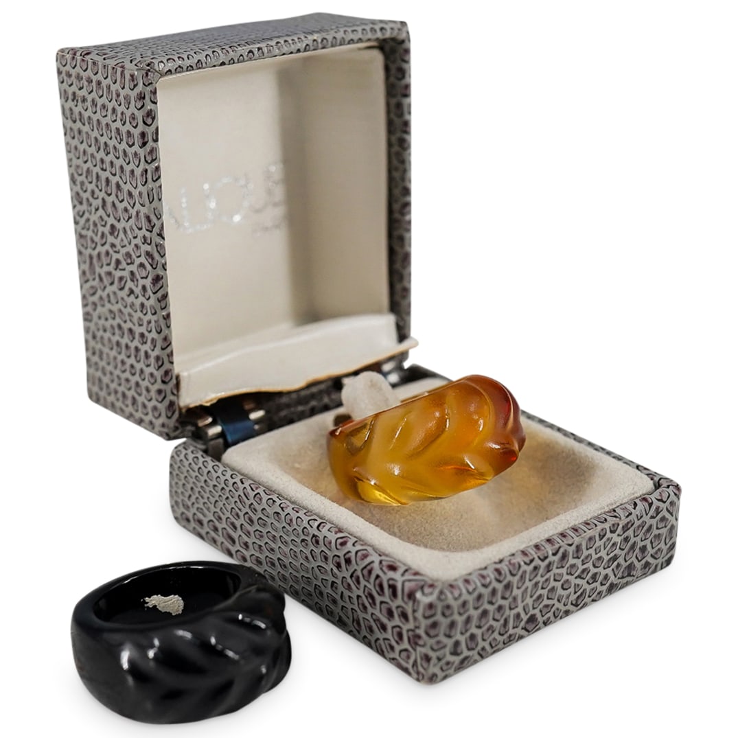 (2 Pc) Lalique Carved Glass Rings: DESCRIPTION: Set of 2 Lalique carved glass rings, one amber tone glass, one black glass. Signed "Lalique France" on band. Includes one Lalique ring box. CIRCA: 20th Century ORIGIN: France DIMENSIONS: 