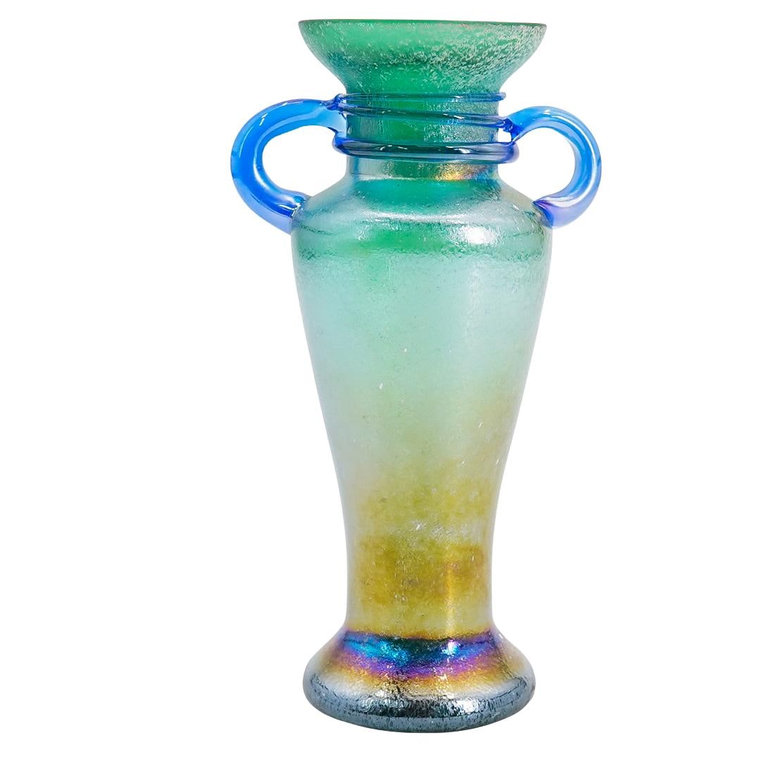 Loetz Iridescent Green Two Handled Glass Vase: DESCRIPTION: Loetz green glass vase with opaque iridescent glaze, and two blue blown glass rounded handles. CIRCA: 20th Century ORIGIN: Austria DIMENSIONS: H: 6.5" W: 2.5" L: 3.25" CONDITION: Good con