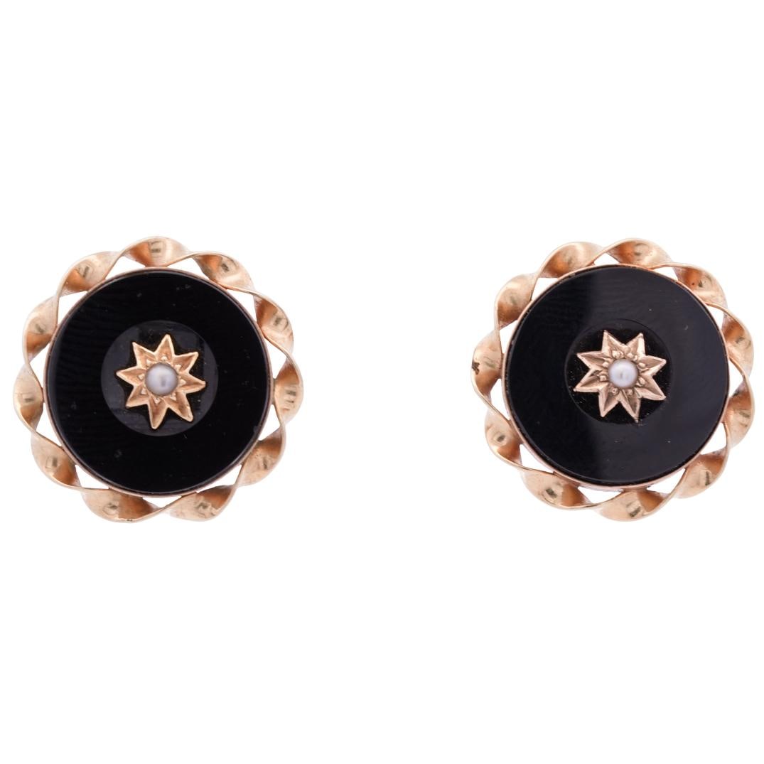 Pair 14k Gold, Onyx, and Pearl Earrings: DESCRIPTION: Pair of 14k gold earrings, featuring circular onyx centerpiece set in a 14k gold ribbon like frame. In the center of the onyx, is a star shaped embellishment with a small round pearl at i