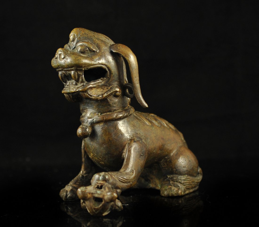 19th Century Chinese bronze foo dog statue: DESCRIPTION: 19th Century Chinese bronze foo dog statue. Bronze foo dog in a sitting position with one paw on top of an ornament. Elongated ears down both sides of the head. Features a hollow design. 