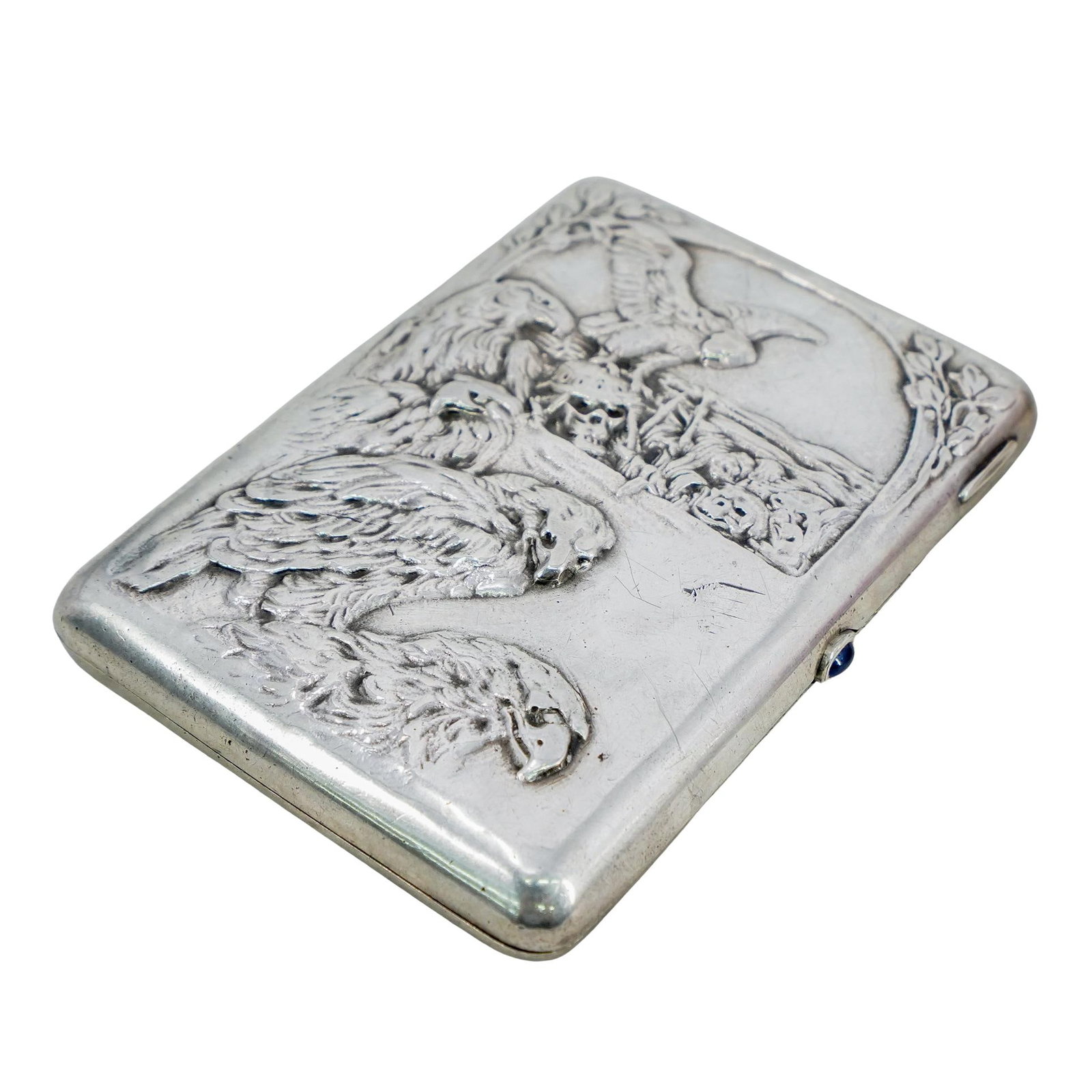 Russian Silver Cigarette Case: DESCRIPTION: Russian 84 zolotnik standard cigarette case, Moscow, featuring relief depictions of skulls and birds of prey, the thumbpiece set with a blue semi-precious stone cabochon. Marked at interi