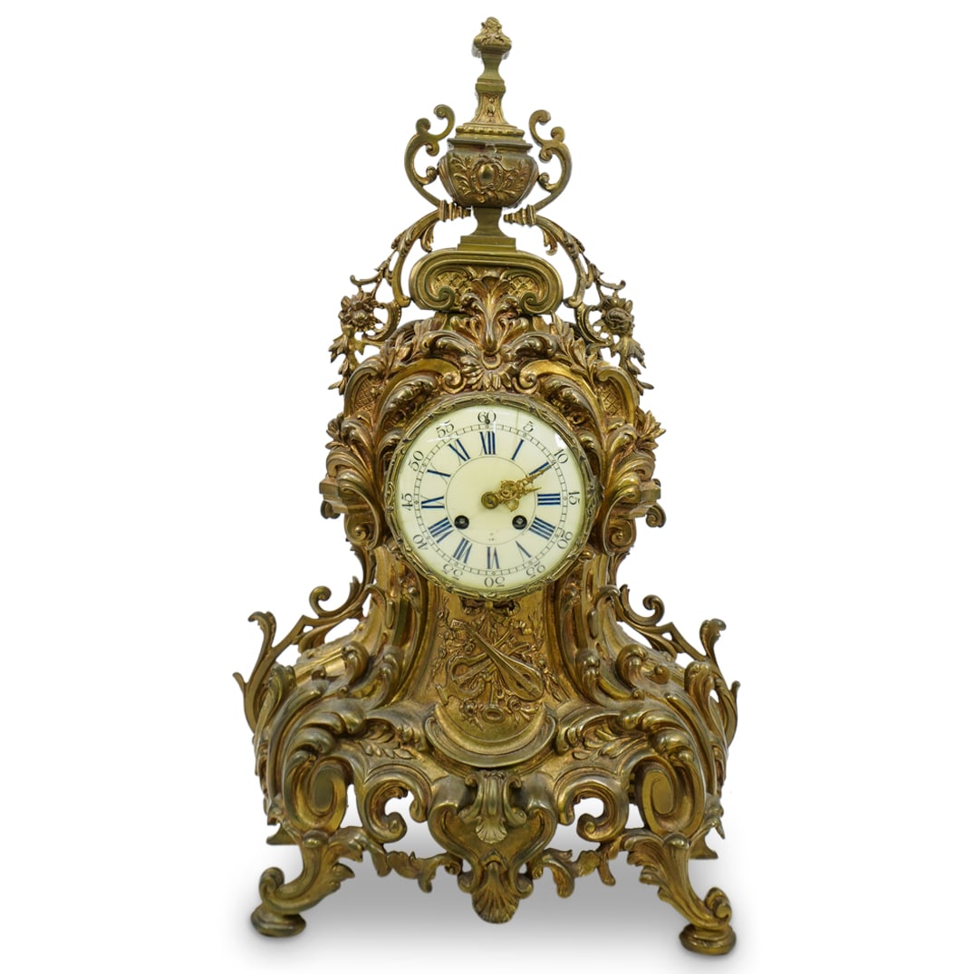 La Gerbe D'Or Gilt Bronze Clock Garniture: DESCRIPTION: La Gerbe d'Or gilt bronze clock garniture, featuring a sculptural form with sweeping curves, scrollwork, and floral motifs, and the lower sections includes volute like scroll feet. The cl