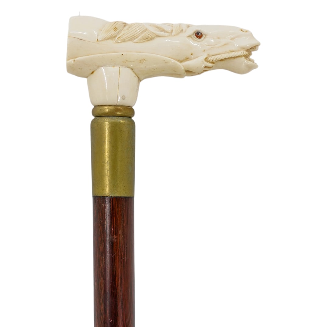 Vintage wood and Carved Bone Equestrian Handle: DESCRIPTION: A vintage cane comprised of a wooden foundation, fitted with a carved bone handle depicting a horse head, completed with glass eye inserts. CIRCA: Mid-Late 20th Cent. ORIGIN: USA DIMENSIO