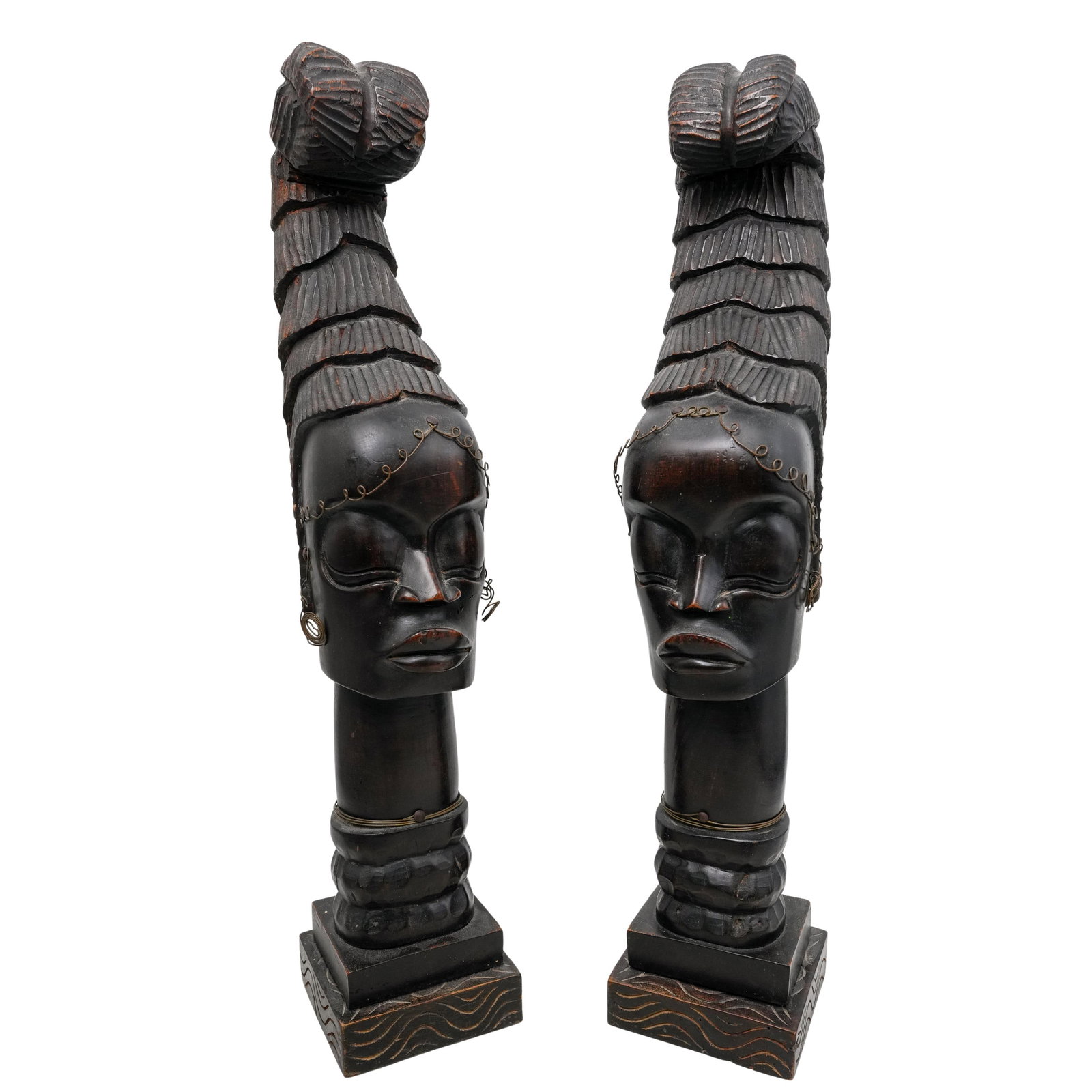 Pair Of African Carved Wood Tribal Busts: DESCRIPTION: This pair of carved wooden sculptures represents African tribal art, featuring human heads with tall, tiered headdresses adorned with textured patterns. Thin metal wire decorations embell