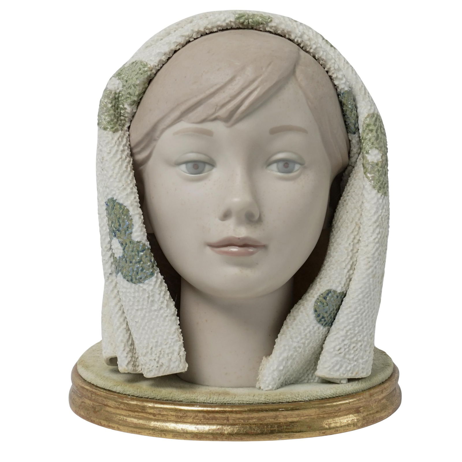 Lladro Porcelain Bust: Lladro Porcelain Bust1969-1985, SpainFinely detailed matte porcelain bust of a woman wearing a textured white headscarf with green and blue floral accents. The head is mounted to an oval gilt-edged wo