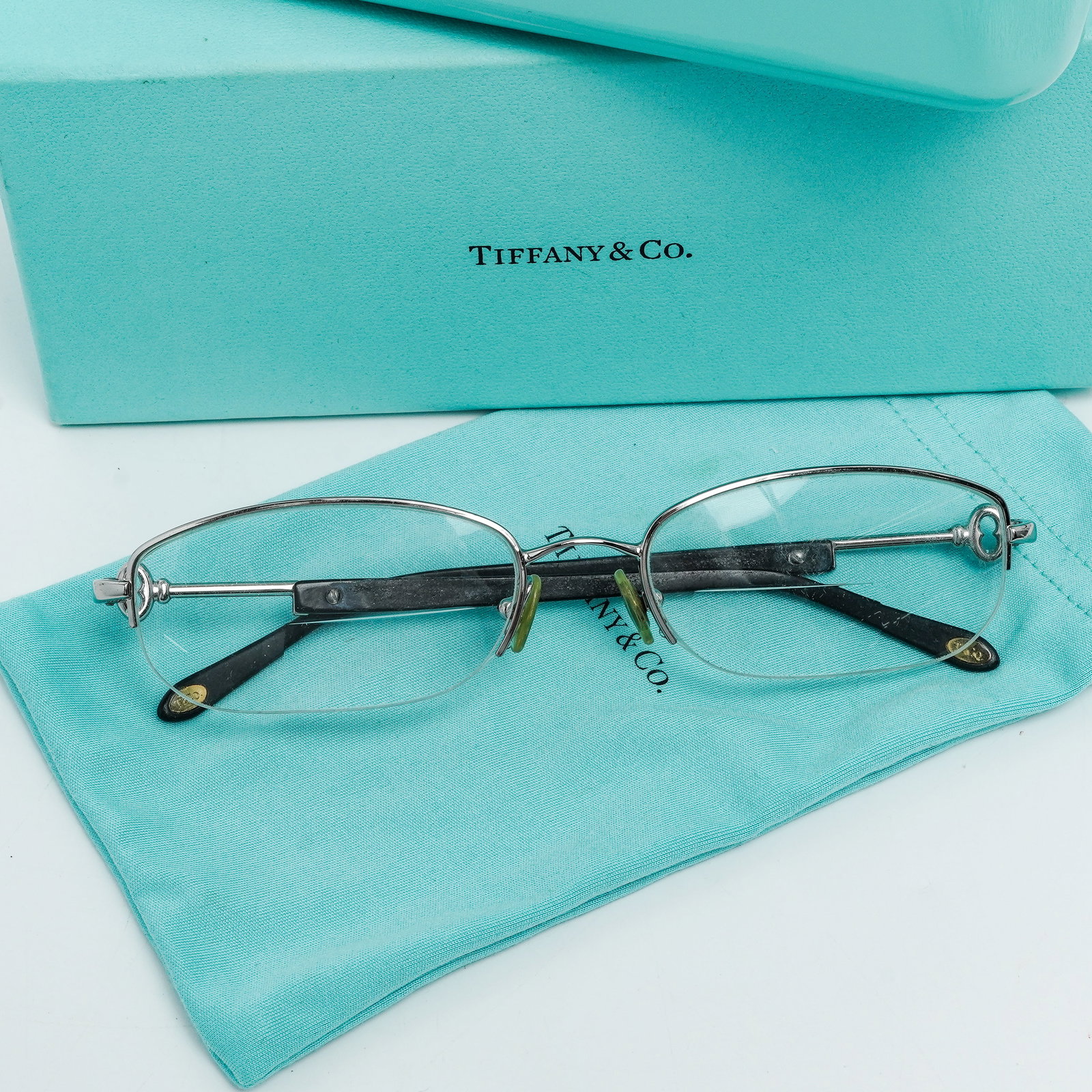 Tiffany & Co. Eyeglasses & Case: Tiffany & Co. Eyeglasses & Case Late 20th Century, USA Designer eyeglasses by Tiffany & Co., featuring a refined rimless-style frame with slender metal arms and subtle gold-tone accents. The temples a