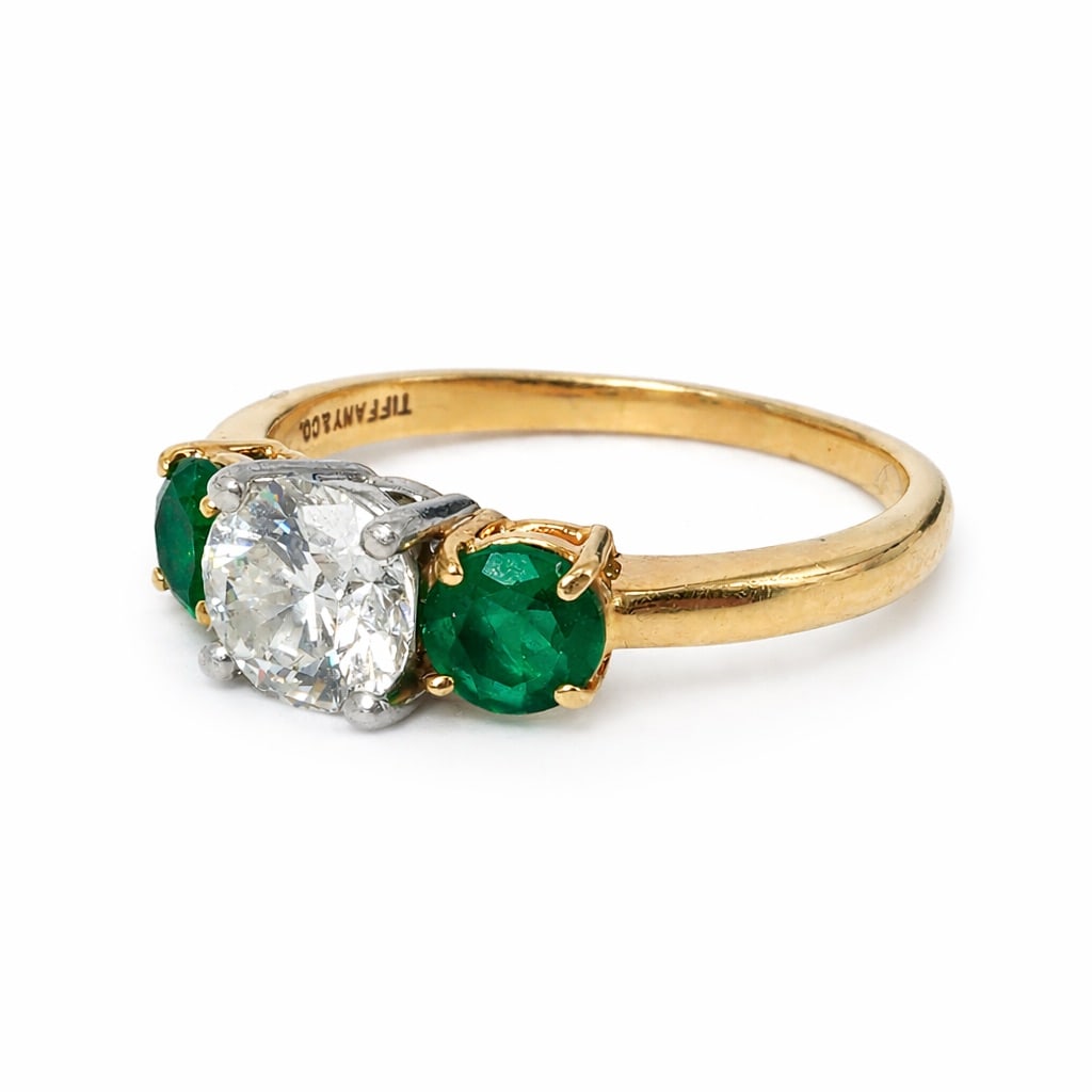 Tiffany & Co. 18k Gold Platinum Diamond & Emerald Ring: Tiffany & Co. 18k Gold Platinum Diamond & Emerald RingCirca: 1990s-2000s, USA.18k yellow gold and platinum Tiffany & Co. three-stone ring, set with an approximately 1.00ct E/F Color, VVS round brillia