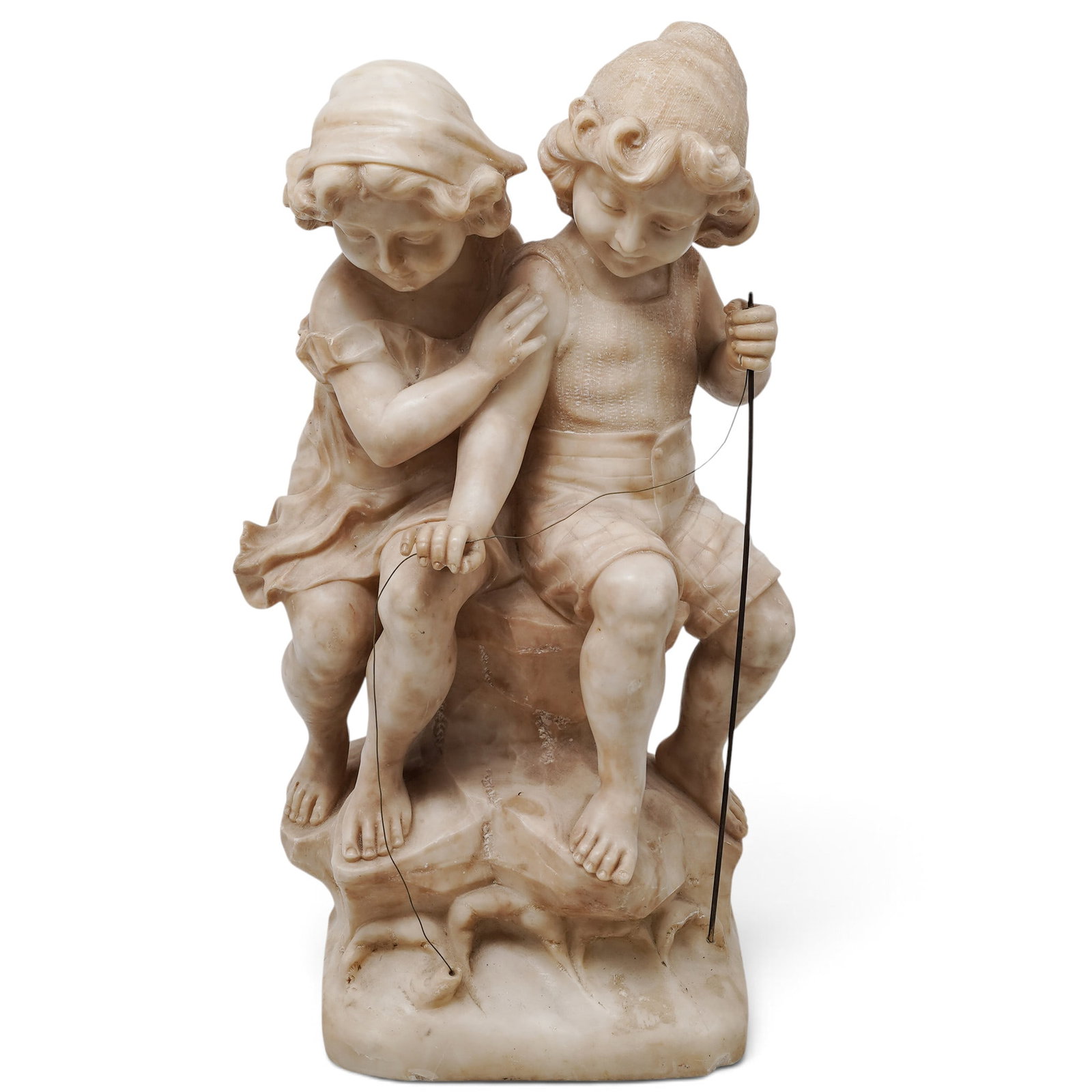 Adolfo Cipriani (Italian, 1880–1930)"I Figli del Pescatore" Alabaster Sculpture: An antique carved alabaster sculpture group depicting a young boy and girl perched upon a rocky outcrop, intently focused on fishing. The figures are masterfully rendered with naturalistic, fluid drap