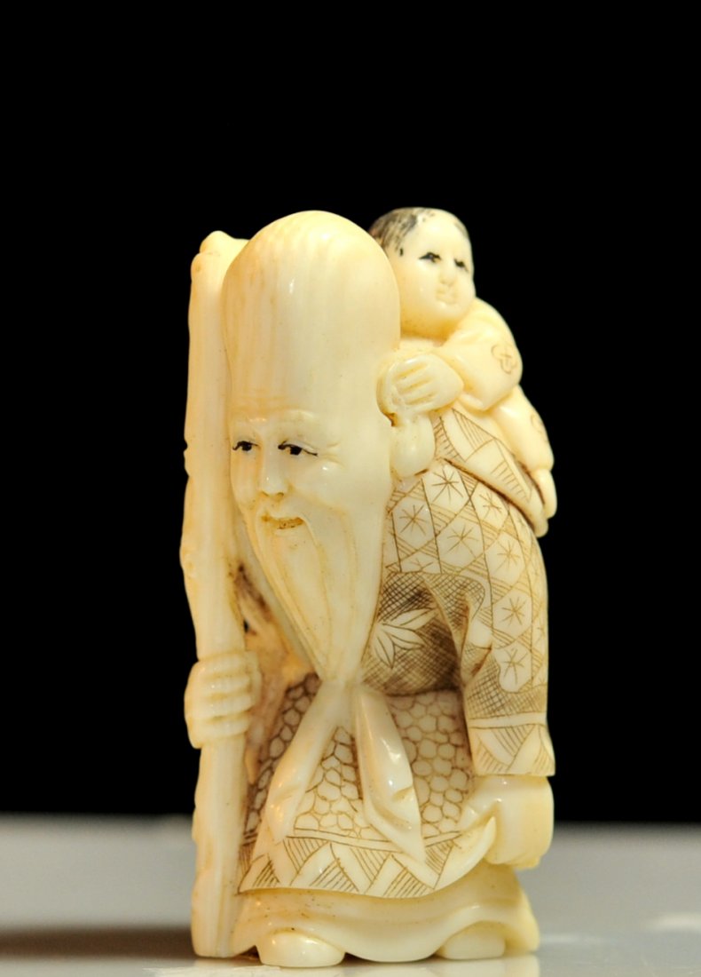 Antique Chinese hand carved "Elder" netsuke: DESCRIPTION: Antique Chinese hand carved "Elder" netsuke. Depicts an elderly man with a walking staff. A small child piggy backs on him while grasping the top of his staff and his left ear. He wears a