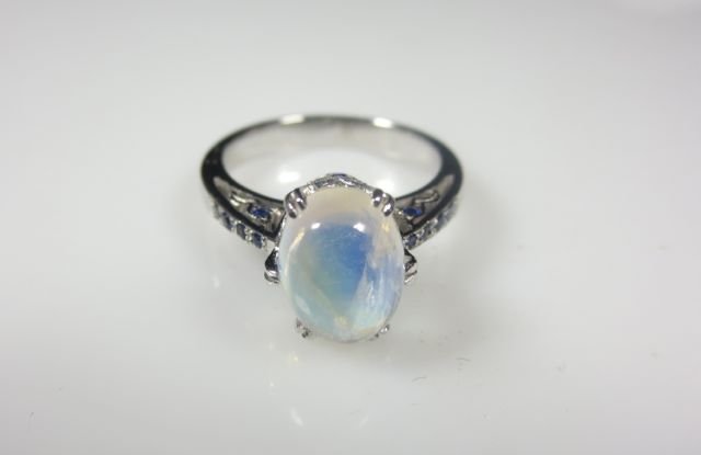 Moonstone, 14k white gold and sapphire ring: DESCRIPTION: Moon stone, 14k white gold and sapphire ring. Center prong mounted cabochon moonstone with an approx weight of 1.50cts in a heavy 14k white gold setting. Delicate filigree style work with