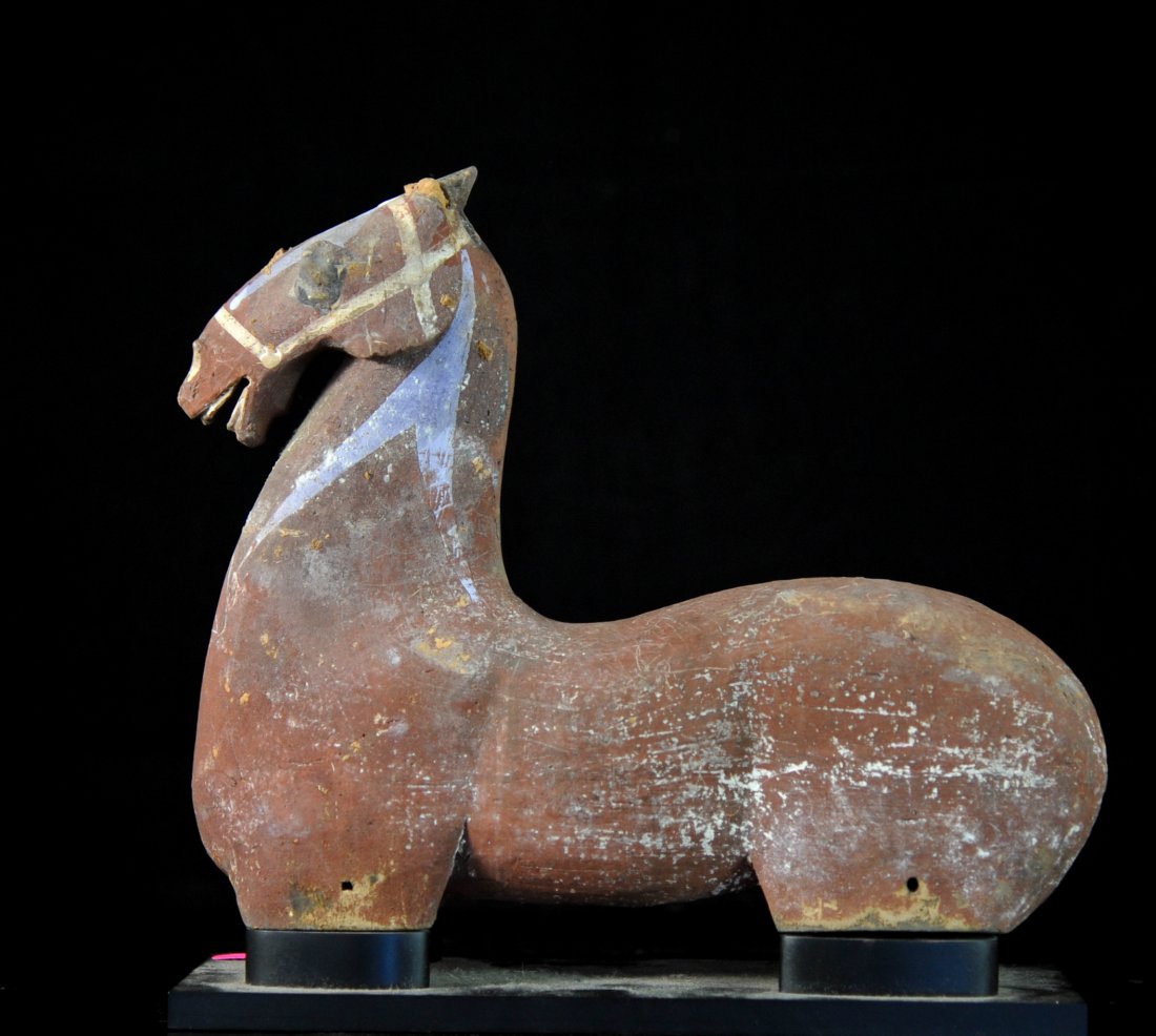 Chinese Han Dynasty ceramic horse on stand: DESCRIPTION: Chinese Han Dynasty ceramic horse on stand. Primitive ceramic design with a rust base color. Painted eyes and bridle. Chips and cracks due to it's age. Mounted on a custom wooden stand. C