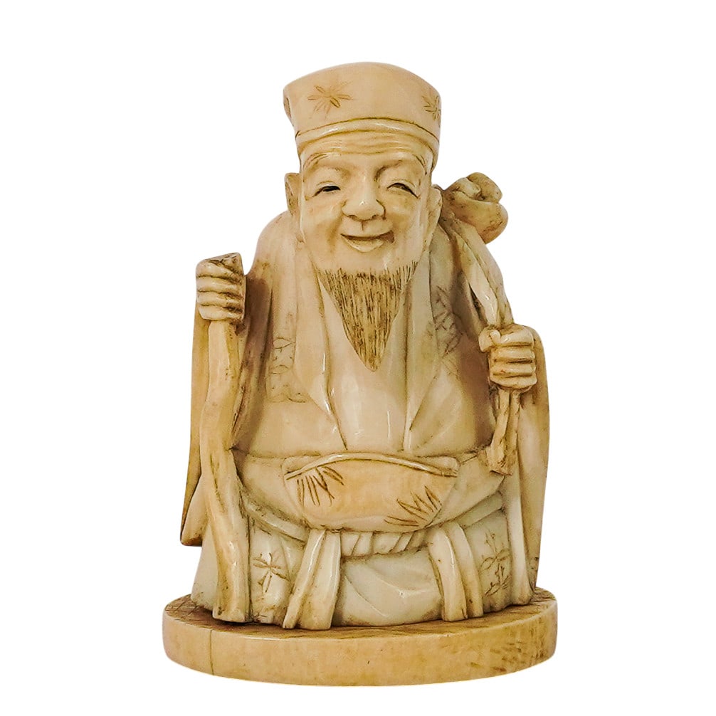 Antique Carved Bone Netsuke Of A Deity: Antique Carved Bone Netsuke Of A Deity 20th Century, Japan Carved bone netsuke depicting a seated deity figure holding a staff and bowl, rendered with finely detailed robes, facial features, and