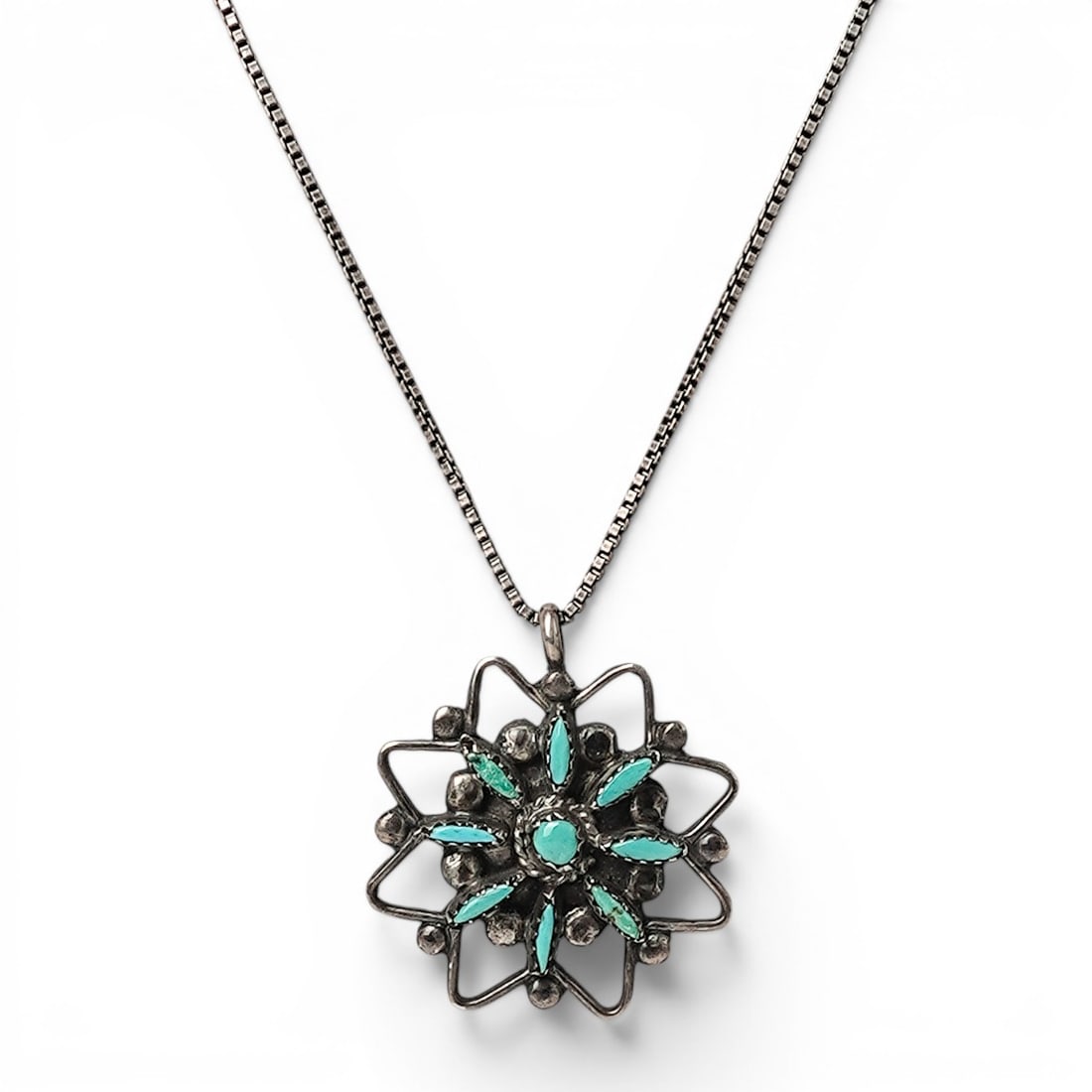 A Zuni sterling silver and turquoise pendant necklace: A Zuni sterling silver and turquoise pendant necklace Late 20th century Unmarked Tests for sterling. A floral pendant with cluster set petit point turquoise surrounding a central round turquoise caboc