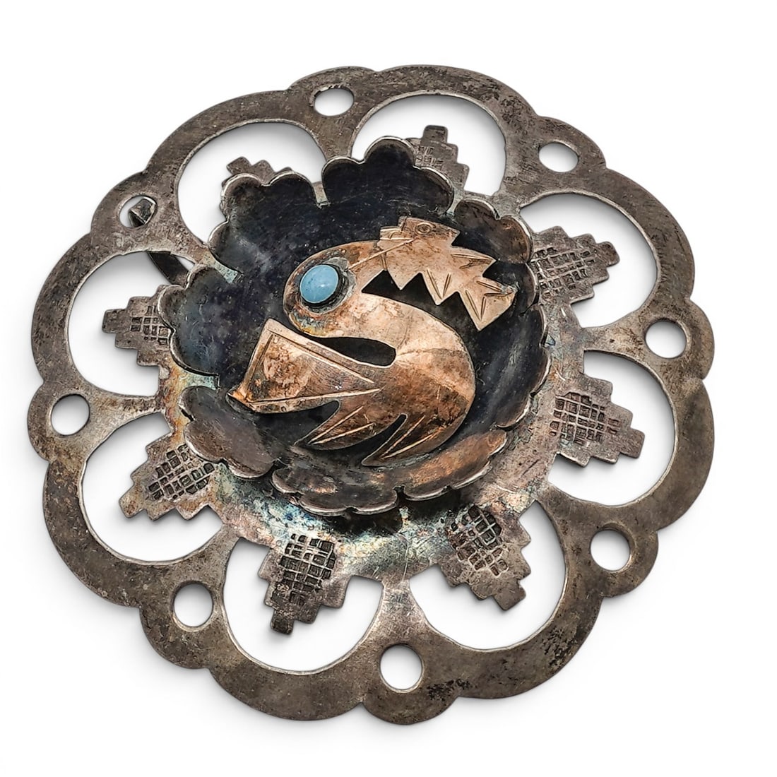 A Peruvian sterling silver and 18K gold bird brooch: A Peruvian sterling silver and 18K gold bird brooch Late 20th century Stamped: .925 / 18K A stylized bird-form overlay brooch accented with a bezel-set round turquoise cabochon and 18K gold overlay de
