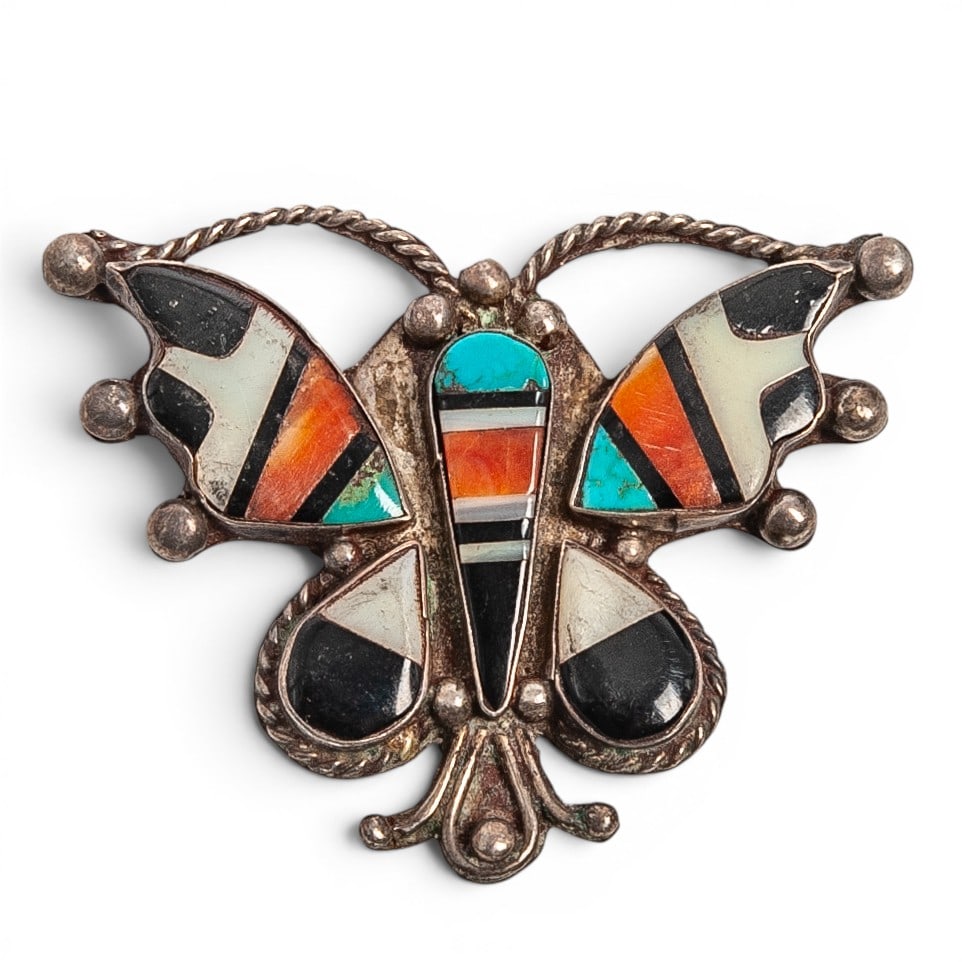 A Zuni sterling silver and multi-stone inlay butterfly brooch: A Zuni sterling silver and multi-stone inlay butterfly brooch Late 20th century Unmarked. Tests for sterling. A butterfly-form brooch with geometric channel inlay of turquoise, mother of pearl, jet, a