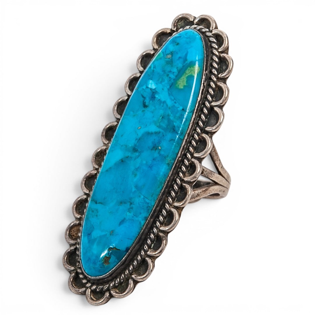A Southwest sterling silver and turquoise ring: A Southwest sterling silver and turquoise ring Late 20th century Stamped: Sterling A split-shank ring set with an elongated oval turquoise cabochon in a serrated bezel, with twisted wire and scalloped