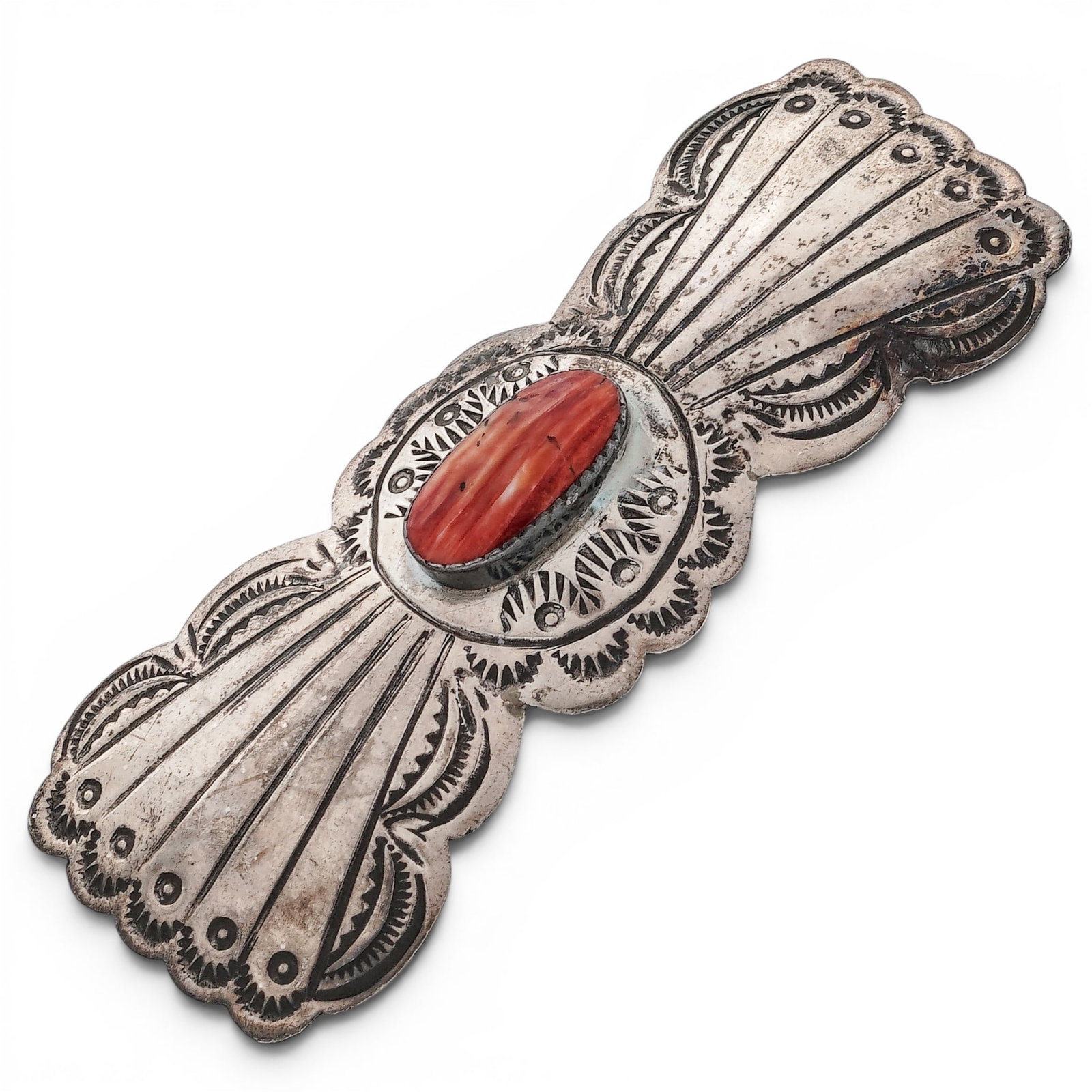 A Southwest sterling silver and coral hair barrette: A Southwest sterling silver and coral hair barrette Late 20th century Stamped: Sterling A concho-form hair barrette centered by an oval coral cabochon in a smooth bezel, with hand-stamped fan and scal