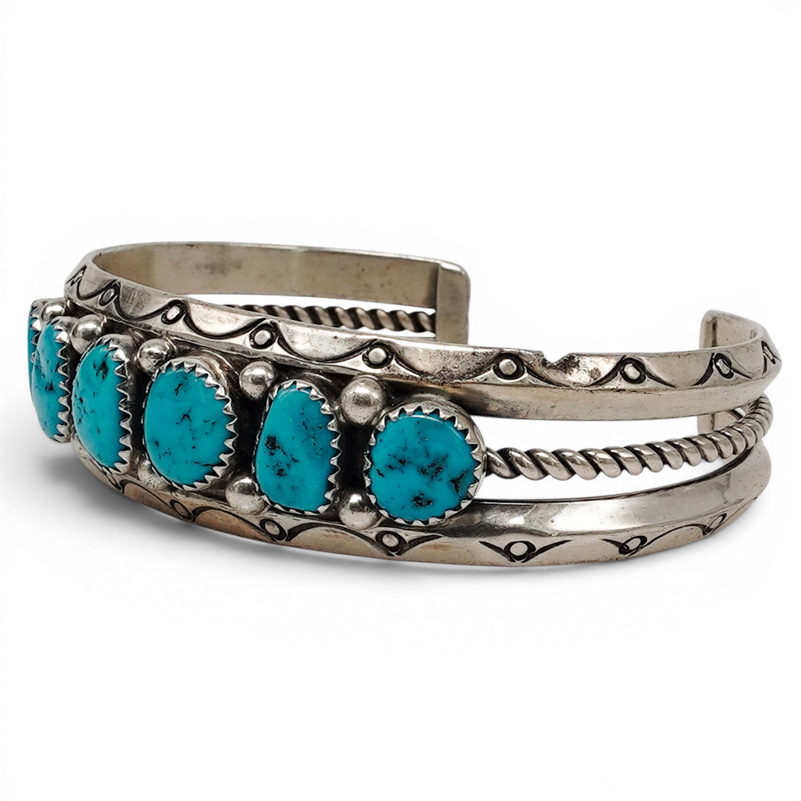 A Sarah Curley Navajo Silver And Turquoise Six Stone Cuff Bracelet: A Sarah Curley Navajo Silver And Turquoise Six Stone Cuff Bracelet Late 20th century Stamped: S.C. / Sterling. A cuff bracelet with six oval bezel set turquoise cabochons separated by applied silver b